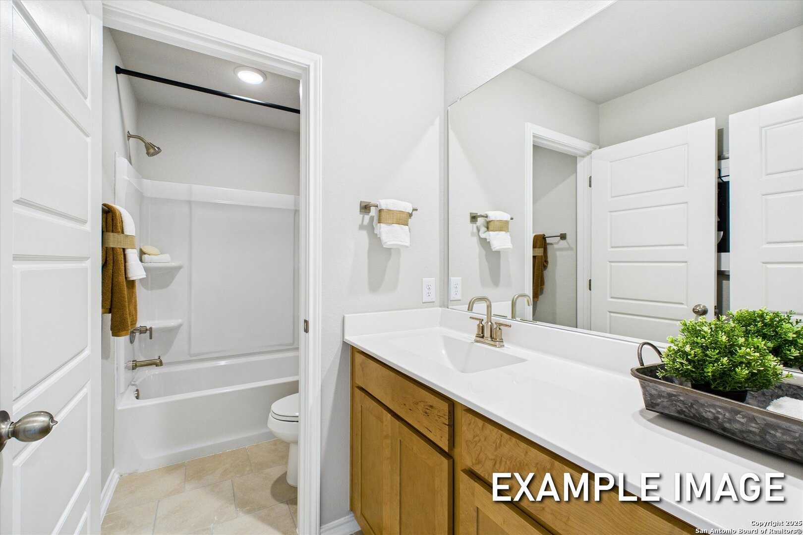 Bright secondary bathroom with white bathtub, single vanity sink, and mirror in Davidson Homes The Sabine C, San Antonio, Texas