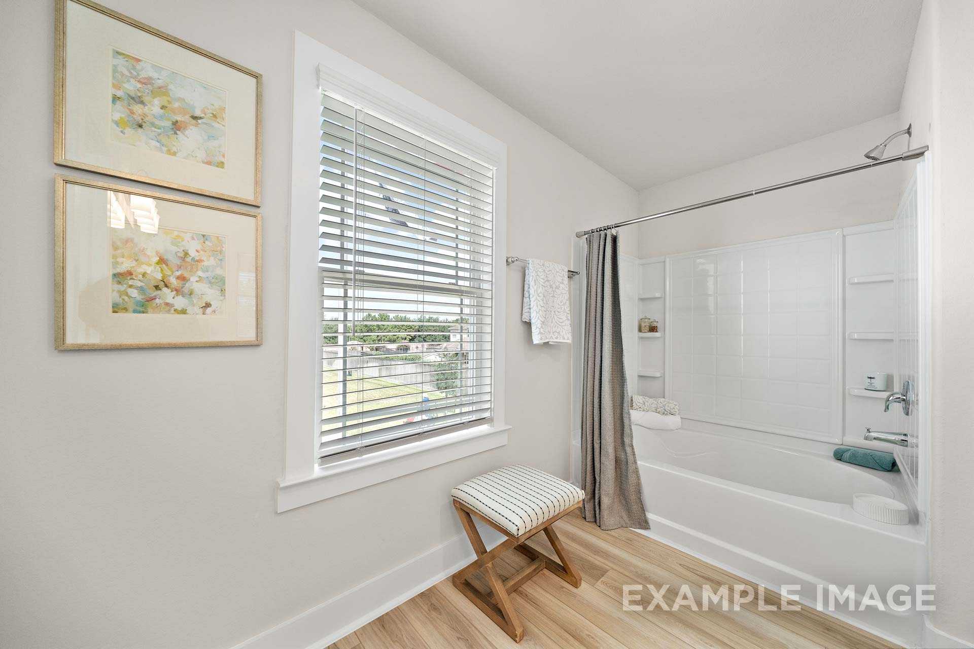Spacious master bathroom in The Lily A with white tiled shower, soaking tub, window blinds, and artwork accents