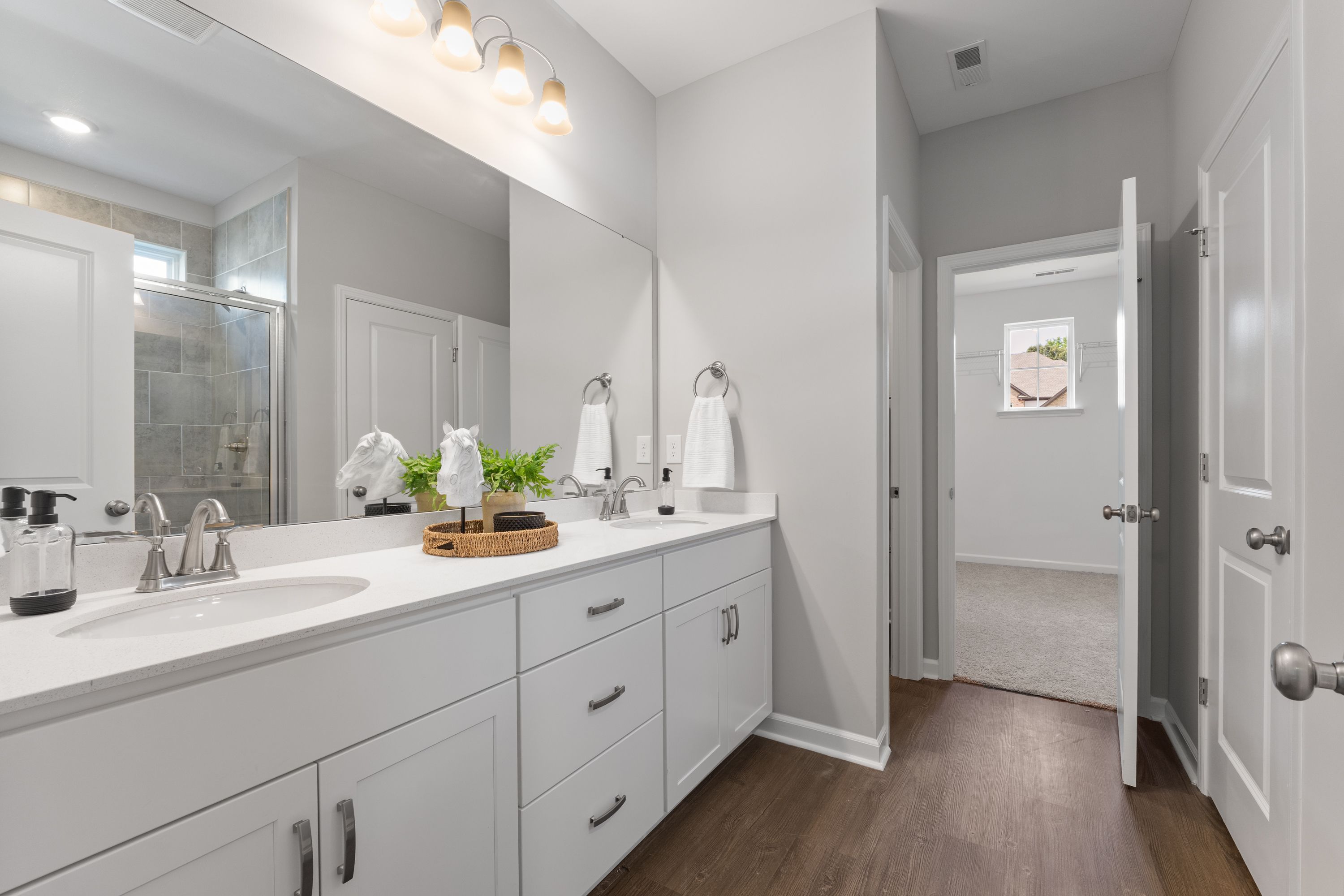 Spacious master bathroom in The Avalon E with white double vanity, large mirrors, walk-in shower, and neutral gray tones