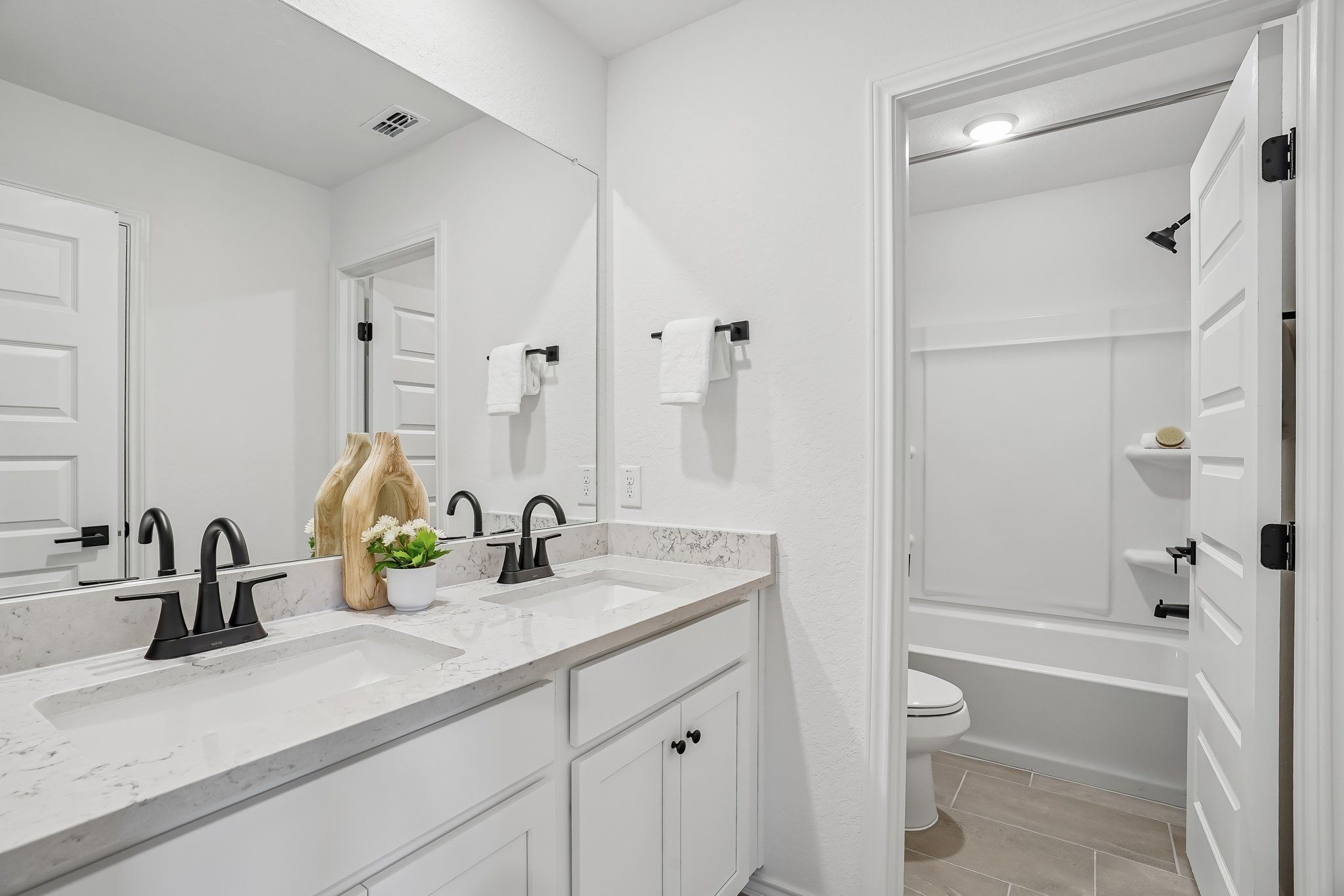 Modern double vanity bathroom at Fairway Crossing in Converse, TX with white cabinetry, quartz countertops, and black fixtures.