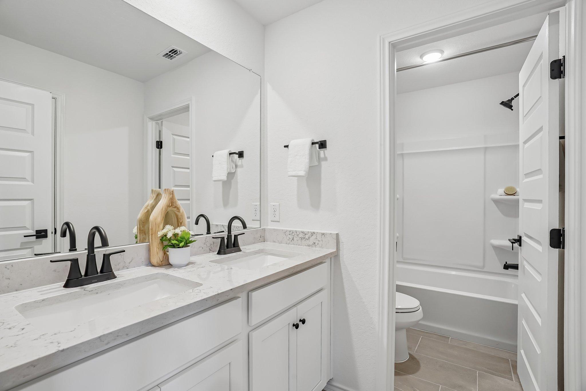 Modern double vanity bathroom at Fairway Crossing in Converse, TX with white cabinetry, quartz countertops, and black fixtures.