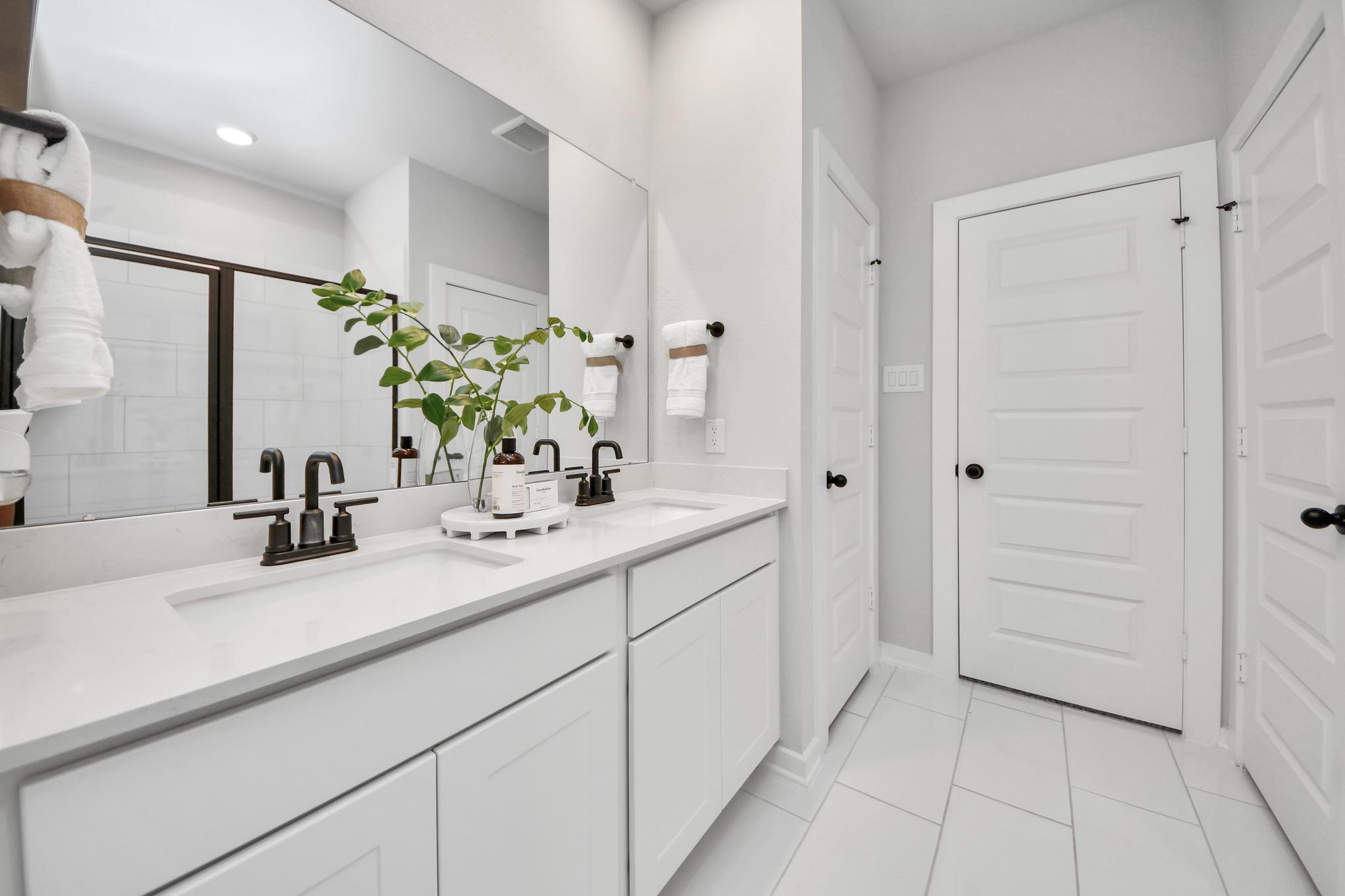 Modern double vanity bathroom at Robins Landing in Houston, Texas by Davidson Homes with white cabinets and dark fixtures.