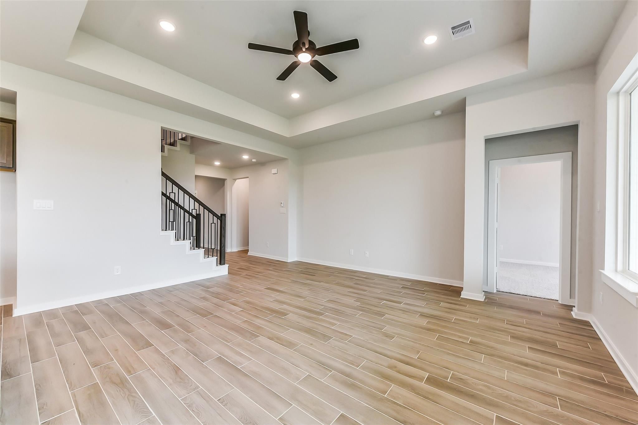Spacious two-story entry with open black-railed staircase, wood-look tile floors, and tray ceiling fan in Davidson Homes Sequoia C, Crosby TX