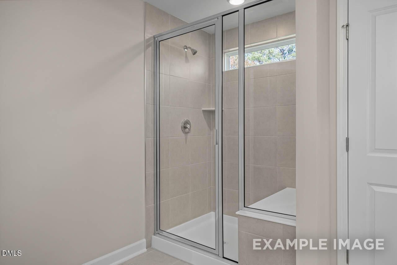 Modern walk-in shower with frameless glass door and neutral tile surround in master bathroom of Davidson Homes The Graham plan, Fuquay-Varina, NC