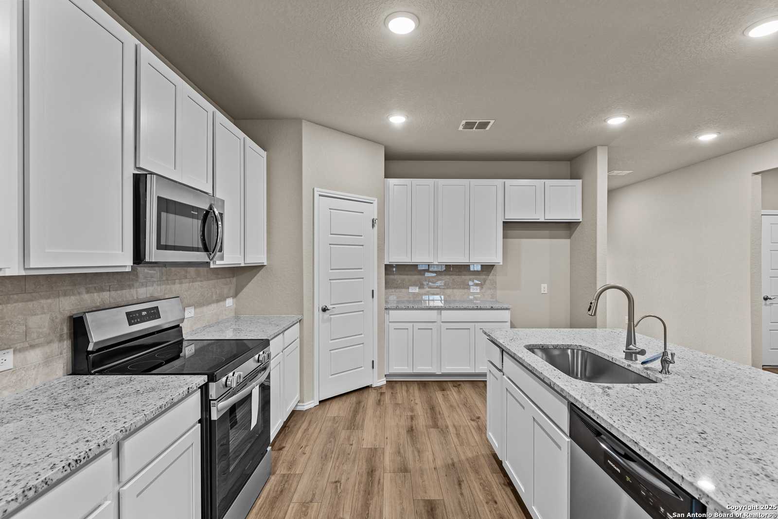 Modern white kitchen with granite island, stainless appliances, subway tile backsplash in Davidson Homes The Douglas F, San Antonio