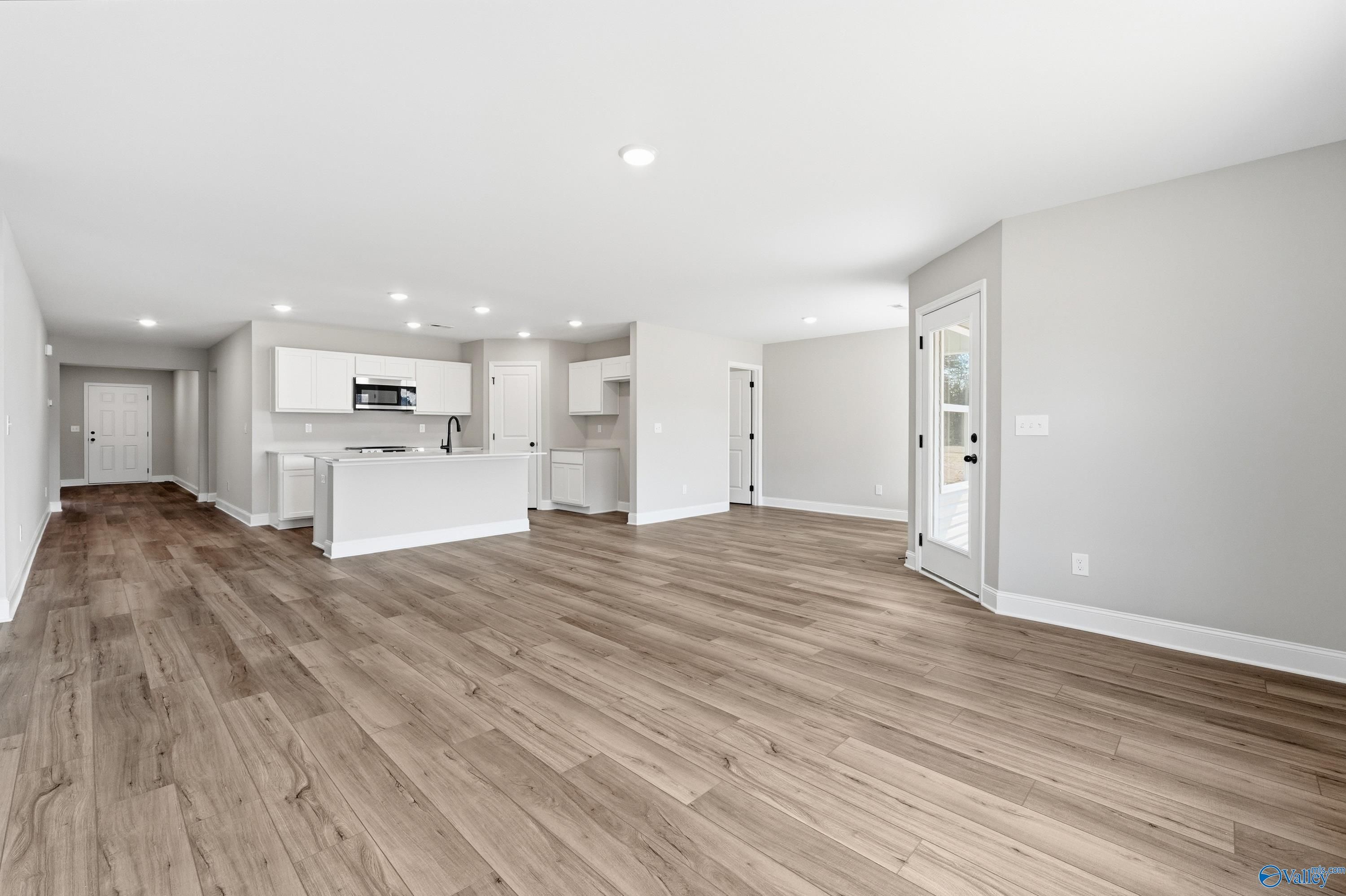 Open-concept great room and kitchen with white cabinets, light wood floors, and French doors in 4-bedroom Daphne V home, Athens, AL