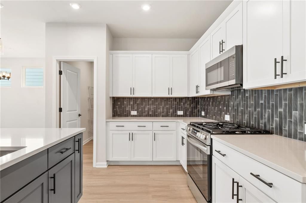 Modern kitchen featuring white shaker cabinets, stainless steel range, and dark subway tile backsplash in The Daphne C, Davidson Homes, Loganville GA
