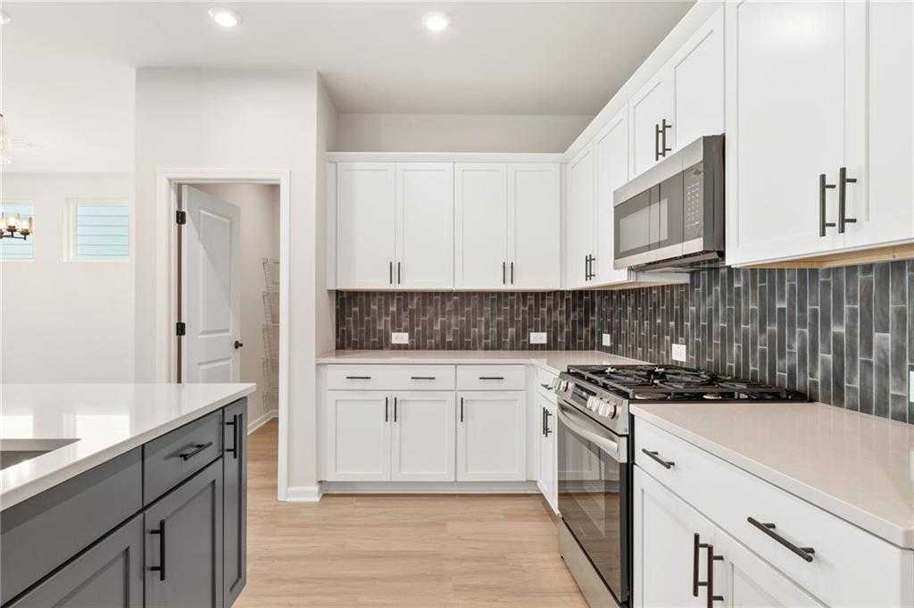 Modern kitchen featuring white shaker cabinets, stainless steel range, and dark subway tile backsplash in The Daphne C, Davidson Homes, Loganville GA