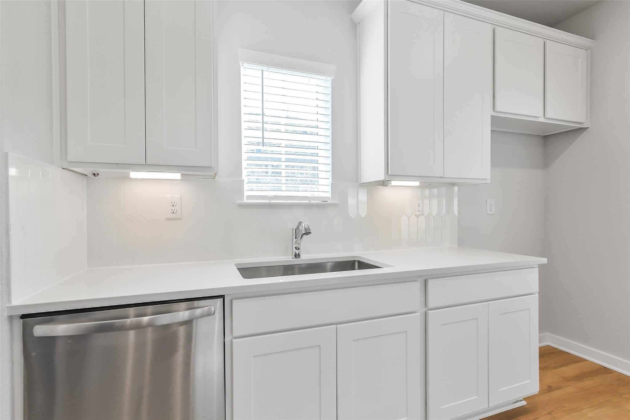 Bright modern kitchen with white shaker cabinets, stainless steel dishwasher, subway tile backsplash in Davidson Homes Trinity F, Magnolia TX