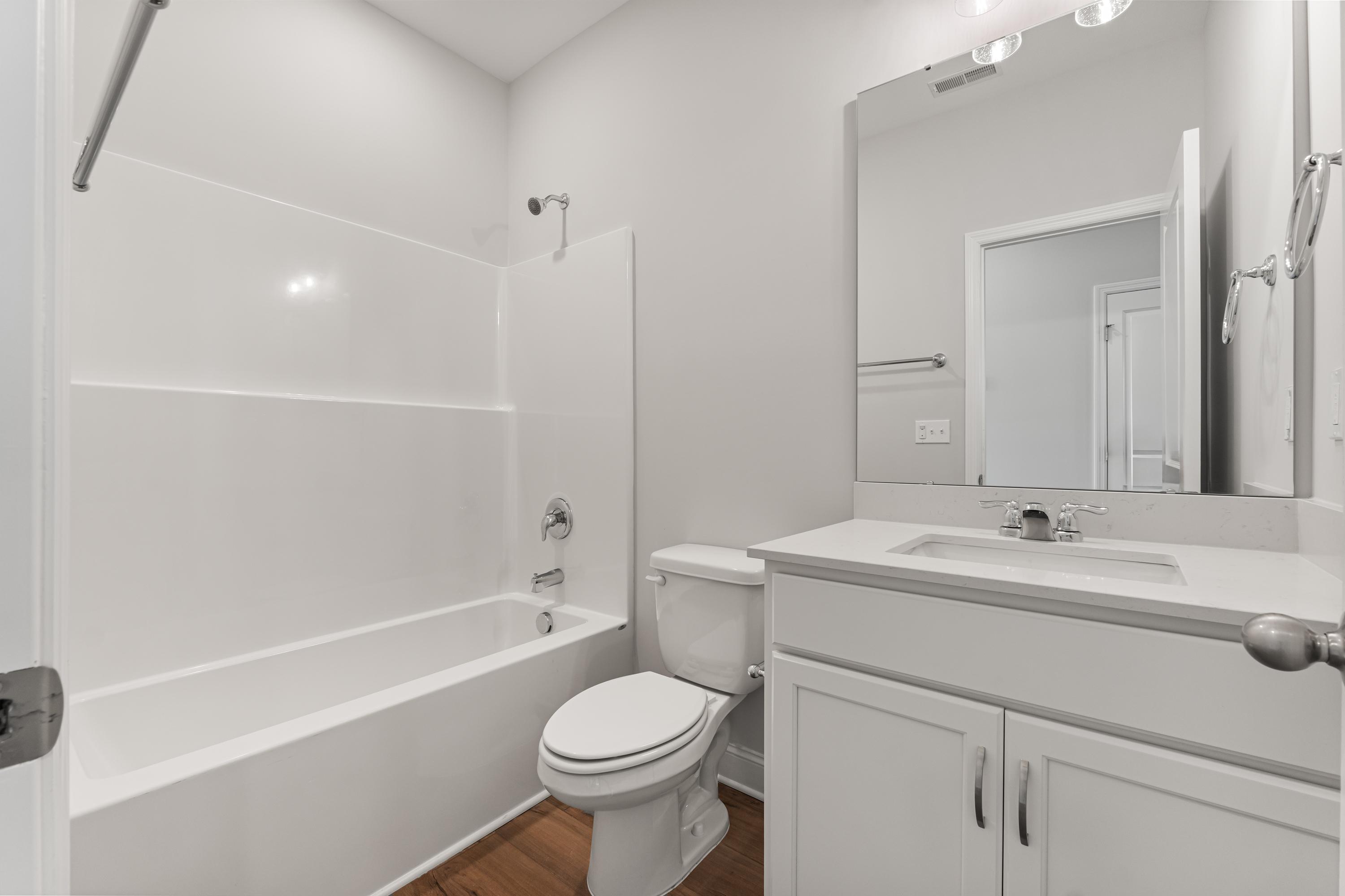 Spacious master bathroom in The Butler by Davidson Homes with white tub, walk-in shower, toilet, vanity, and hardwood floors
