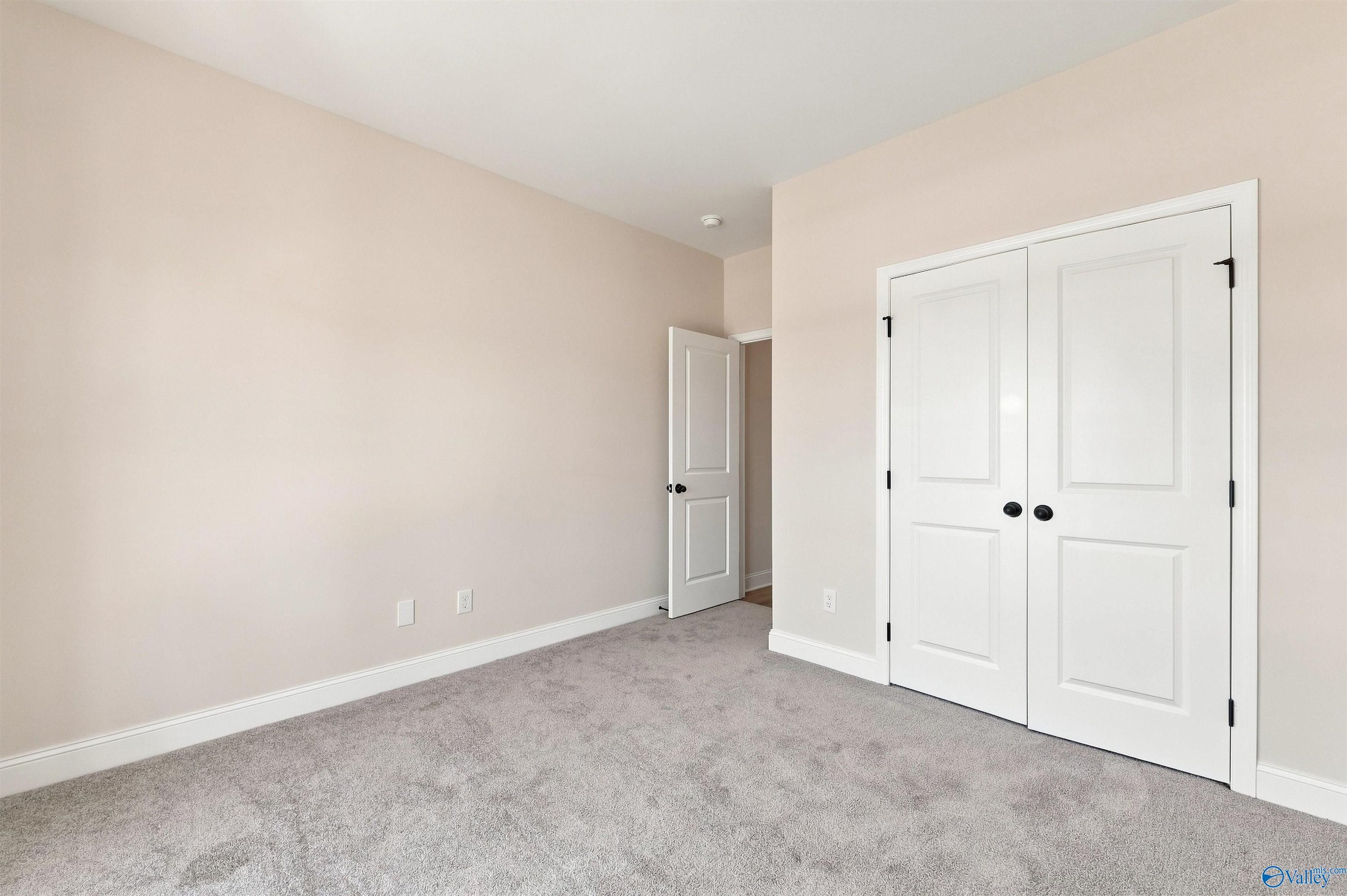 Bright bedroom with plush gray carpet, white double-door closet, and neutral walls in Davidson Homes The Everett B, Ivy Hills, Toney, Alabama