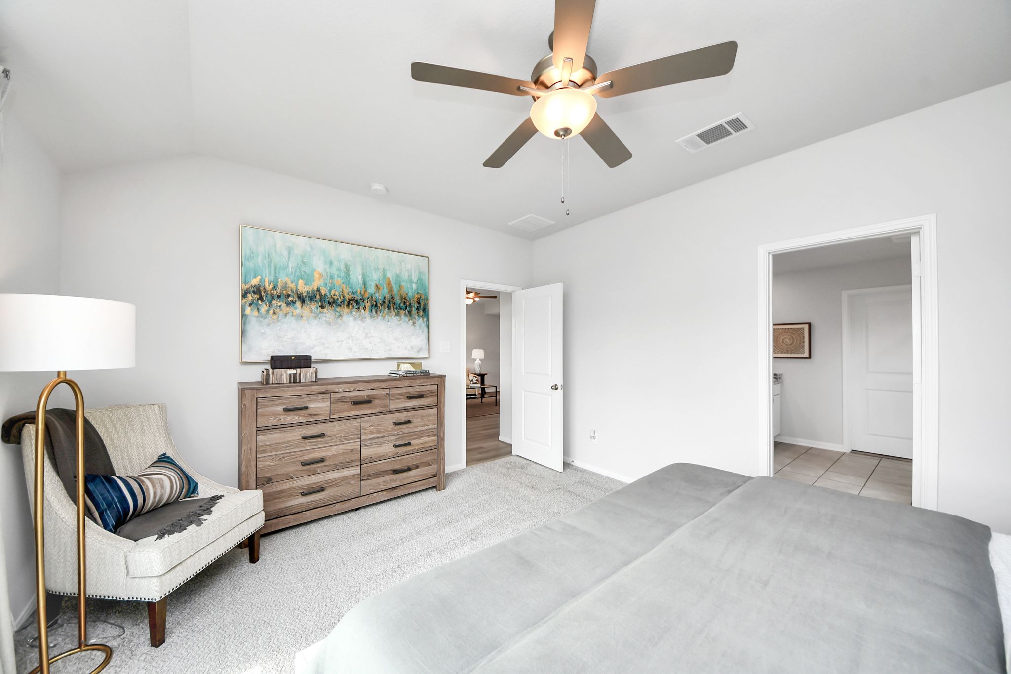 Spacious bedroom at Sunterra in Katy, Texas by Davidson Homes with a cozy reading chair, wooden dresser, and neutral decor.