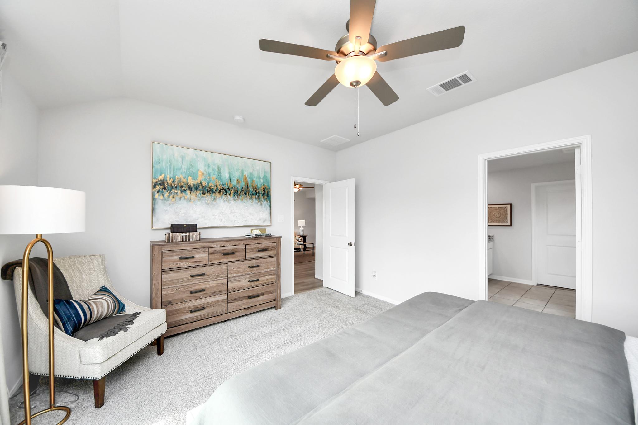 Spacious bedroom at Sunterra in Katy, Texas by Davidson Homes with a cozy reading chair, wooden dresser, and neutral decor.