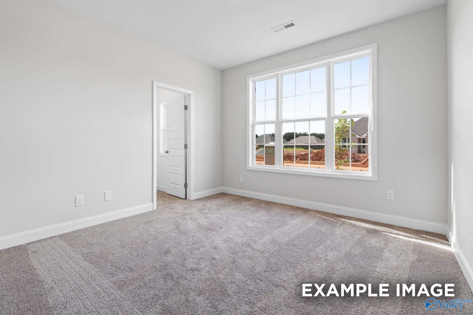 Bright empty bedroom with large windows, gray carpet, light walls in The Montgomery 3-bedroom home, The Meadows, Athens, Alabama
