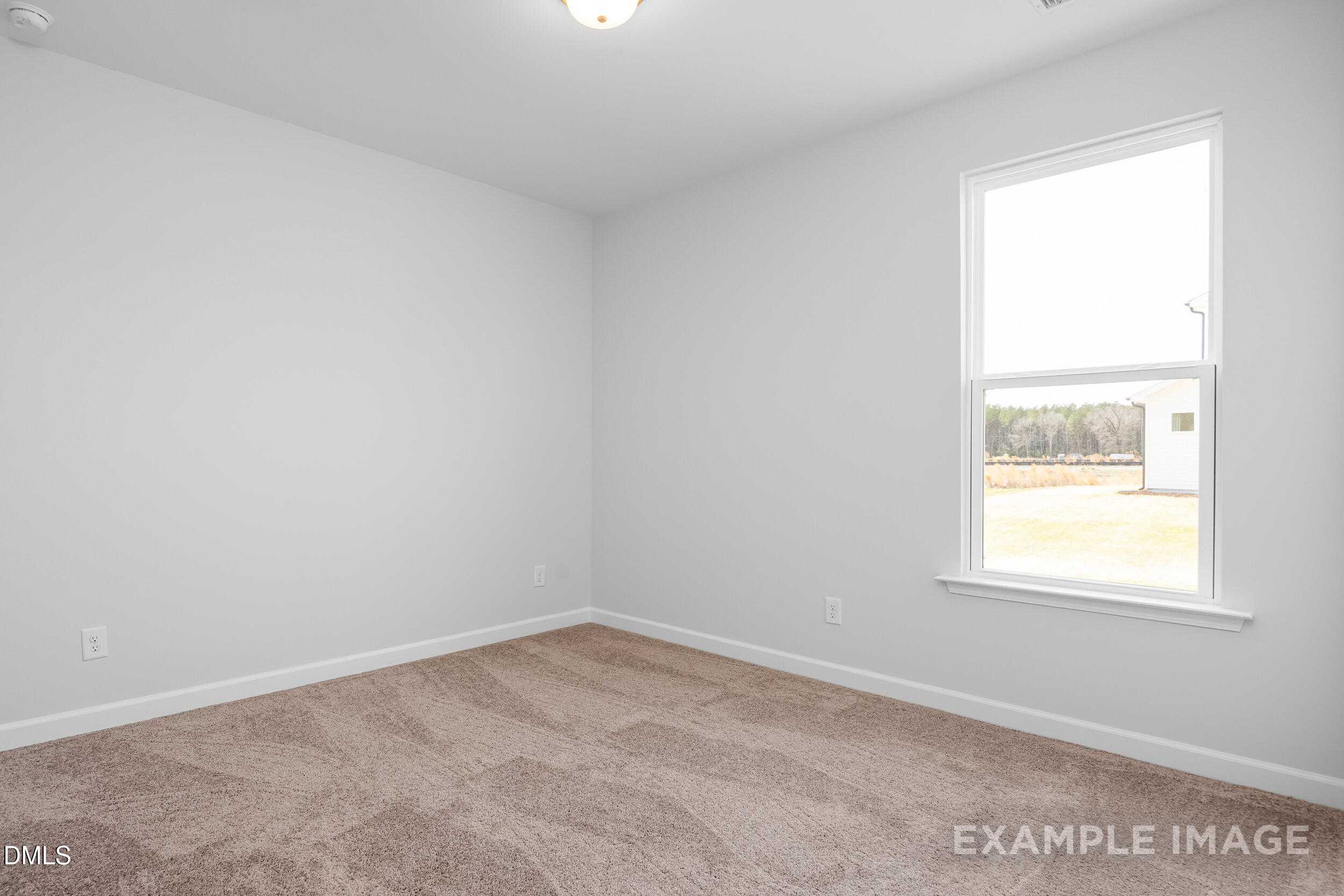 Bright empty bedroom with neutral walls, beige carpet, and large window overlooking yard in The Franklin C home, Lillington, NC