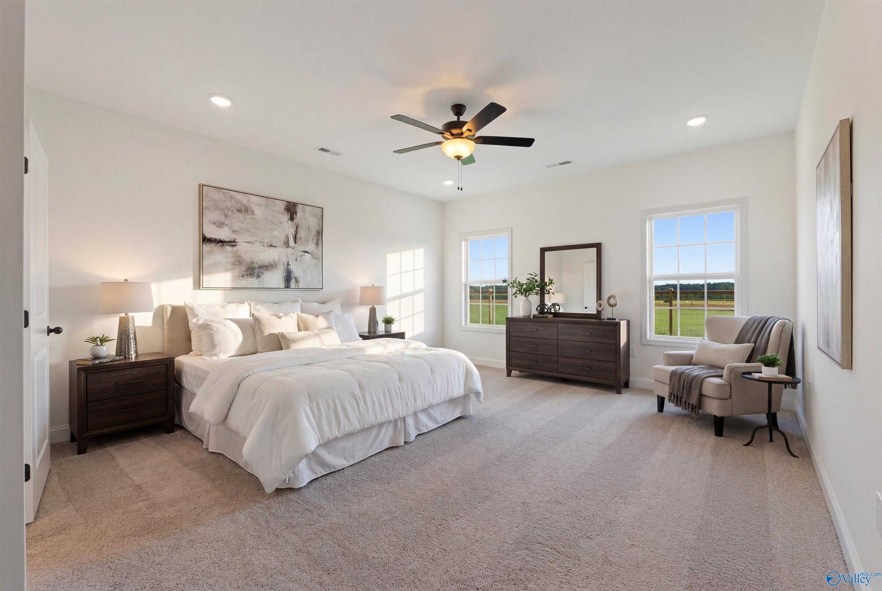 Spacious master bedroom with king bed, white linens, dresser, mirror, and field views through large windows in Davidson Homes The Rockford B, Toney, Alabama
