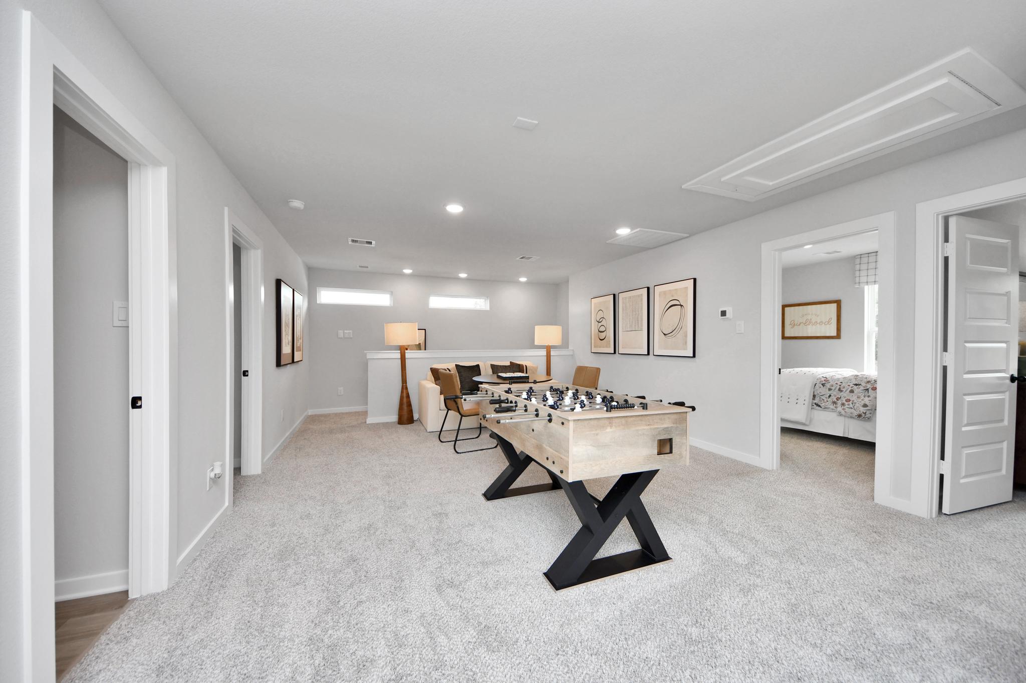 Spacious loft and game room at Robins Landing in Houston, TX by Davidson Homes featuring a foosball table and seating area.