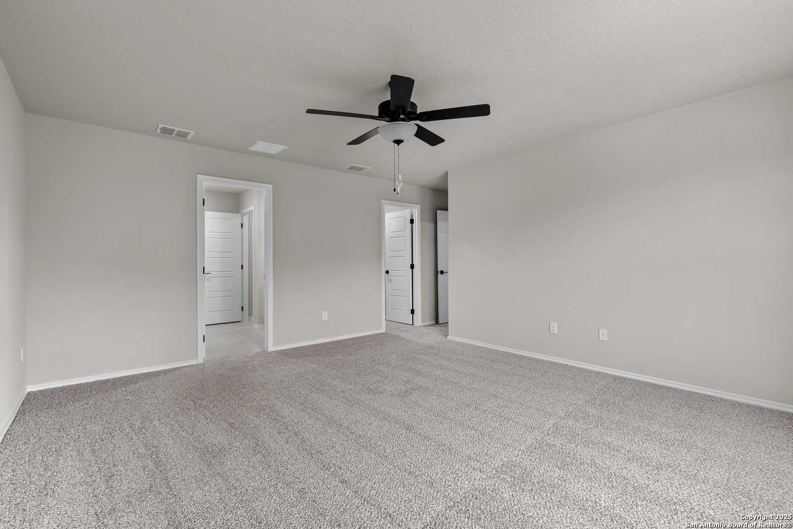 Spacious beige bedroom with ceiling fan, gray carpet, and double doors in Davidson Homes The Murray I, San Antonio