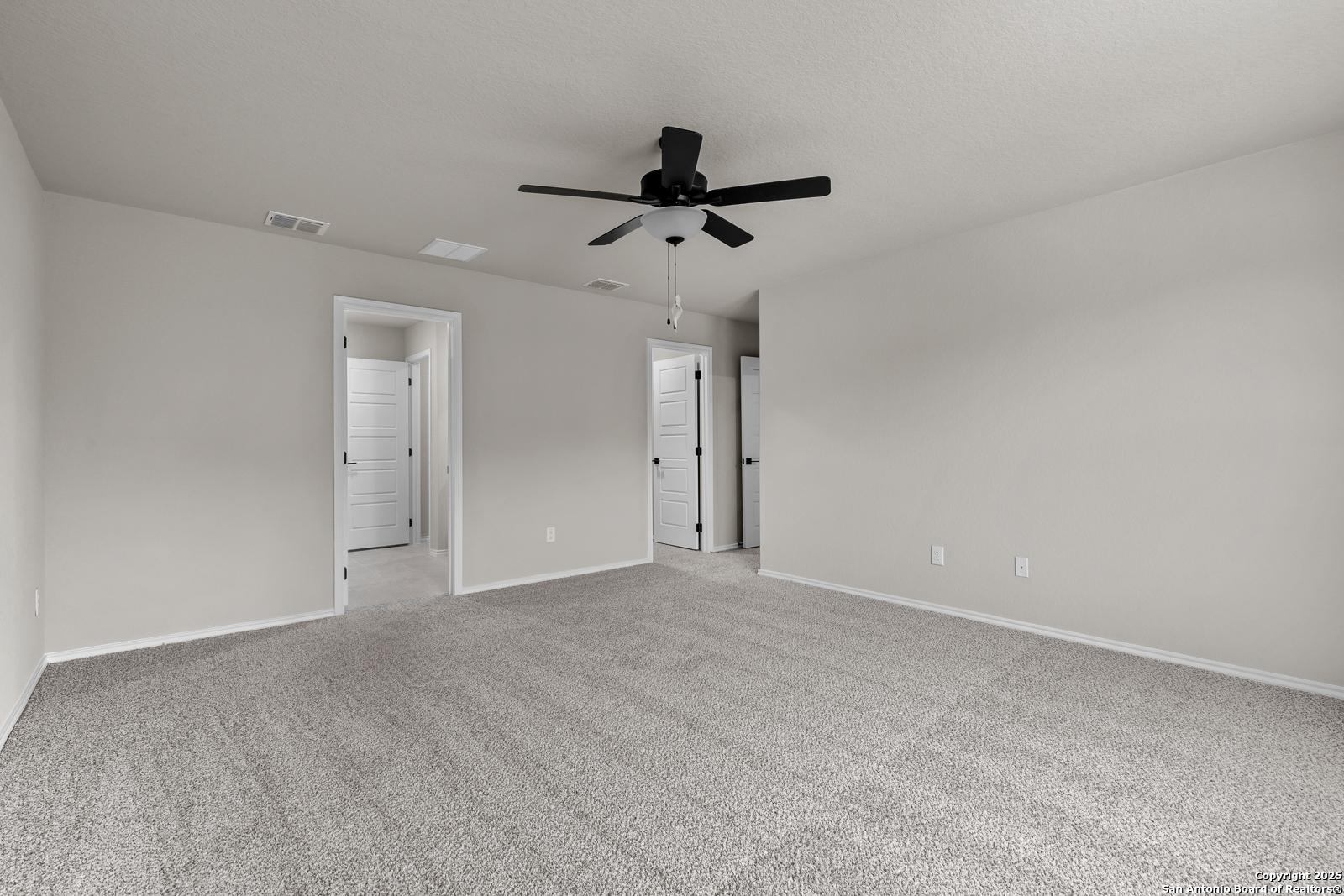 Spacious beige bedroom with ceiling fan, gray carpet, and double doors in Davidson Homes The Murray I, San Antonio