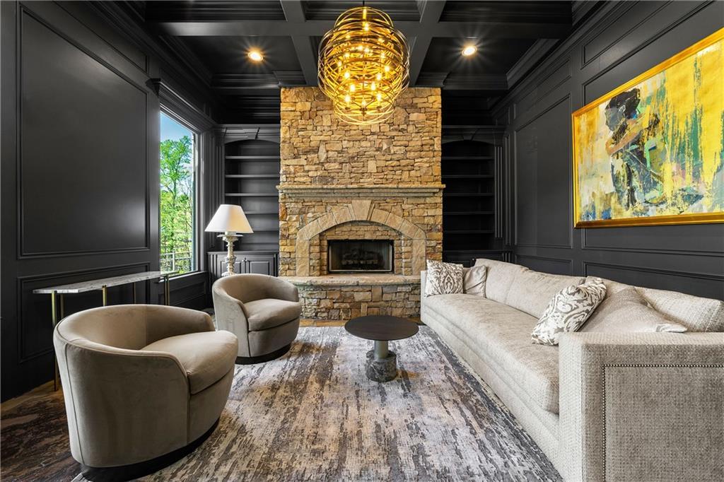 Cozy living room with stone fireplace, dark paneled walls, modern chandelier, beige sofa, gray chairs in Davidson Homes The Ash B, Riverwood, Dallas, GA