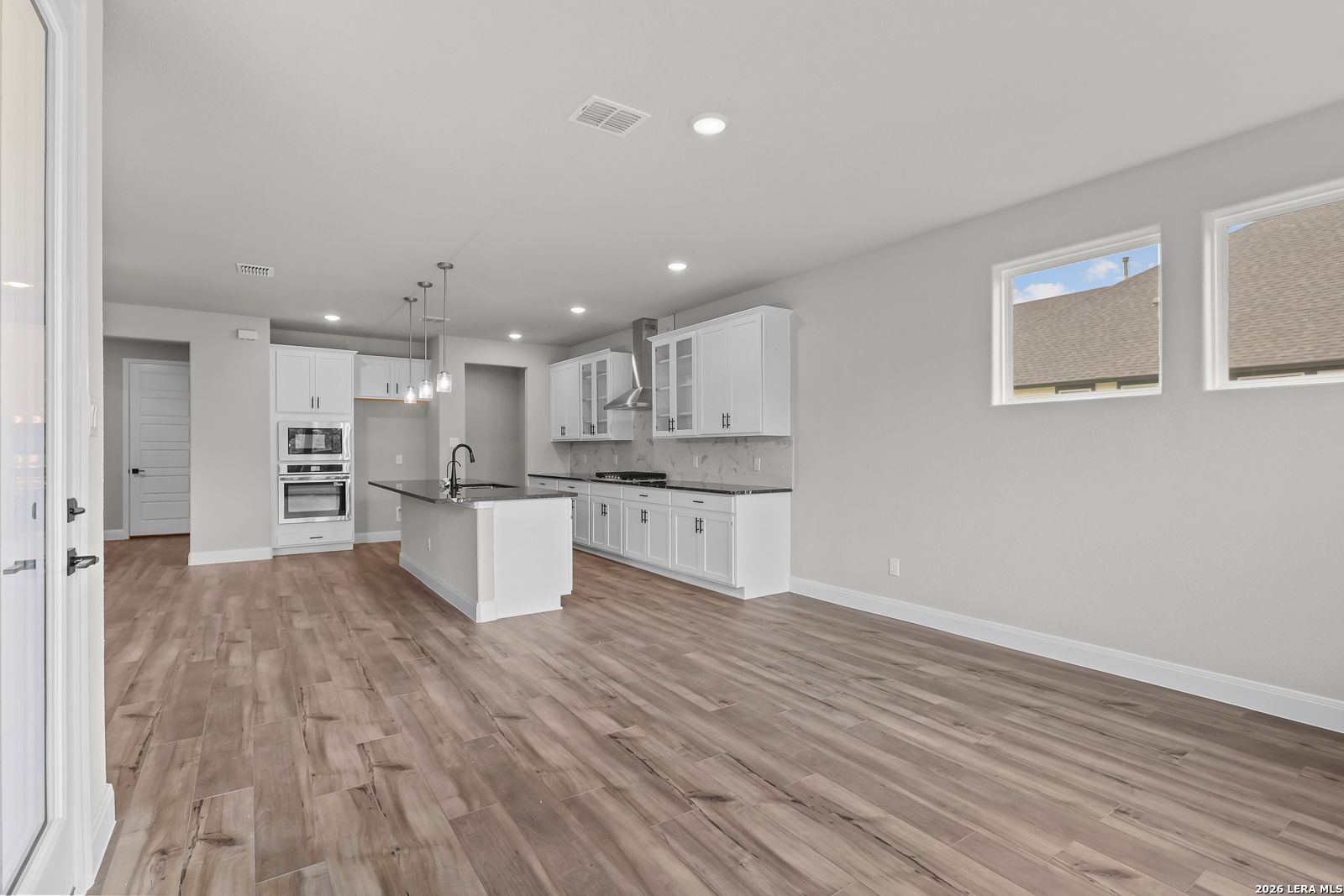 Modern white kitchen with large island, stainless double oven, cooktop, and hardwood floors in Davidson Homes Belmont H, Castroville, TX