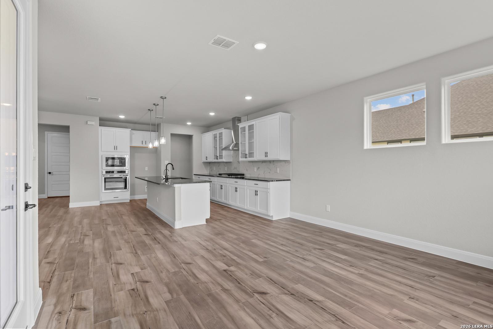 Modern white kitchen with large island, stainless double oven, cooktop, and hardwood floors in Davidson Homes Belmont H, Castroville, TX