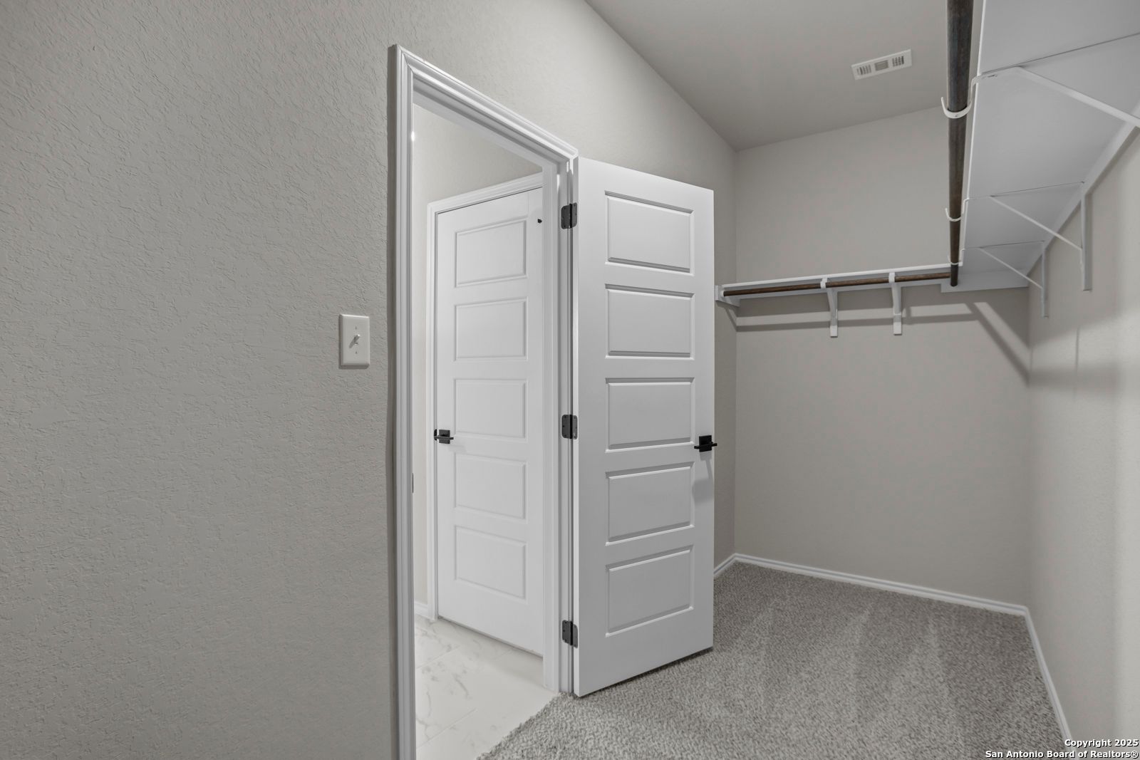 Spacious walk-in closet with open double doors, gray carpet, shelving, and hanging rods in The Daphne H master suite, Seguin, Texas