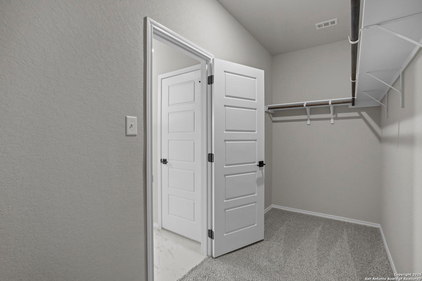 Spacious walk-in closet with open double doors, gray carpet, shelving, and hanging rods in The Daphne H master suite, Seguin, Texas