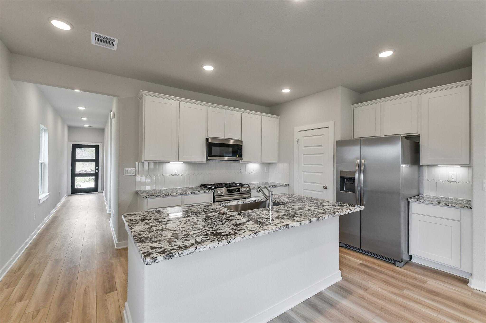 Modern kitchen featuring white cabinets, speckled granite island, stainless steel fridge and appliances in Davidson Homes The Colorado G, Magnolia Texas