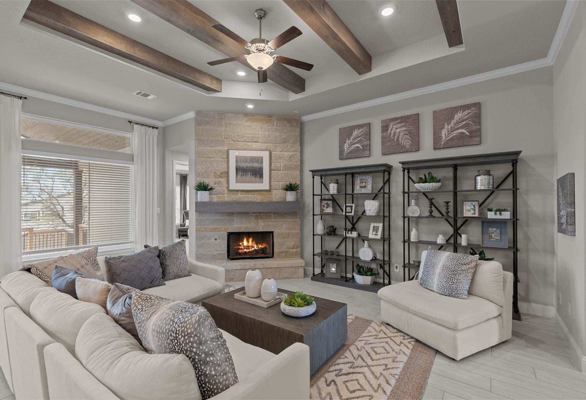 Spacious living room in The Garner A featuring stone fireplace, beige sectional sofa, wooden beams, and built-in bookshelves