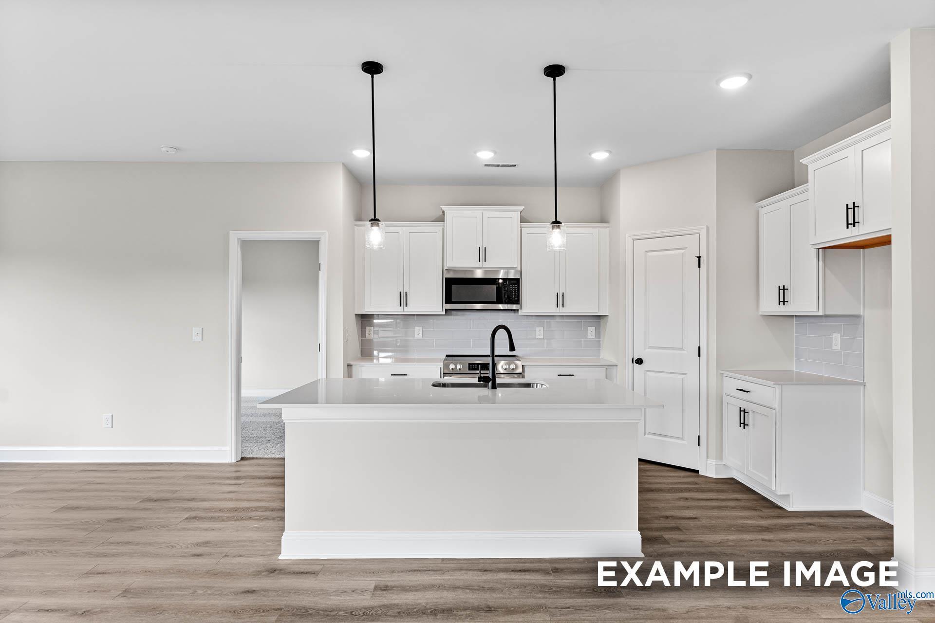 Modern kitchen with white cabinets, center island, and pendant lighting in The Franklin B floor plan at Creekside, Harvest.