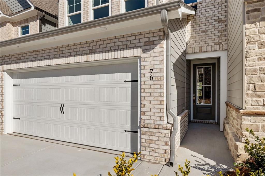 Modern brick exterior with 2-car garage, house number 76, and glass front door in Davidson Homes The Marion A, Winder, Georgia