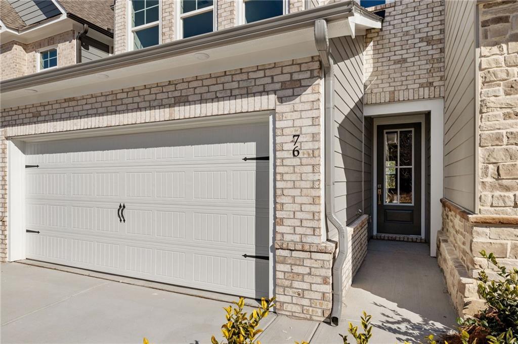Modern brick exterior with 2-car garage, house number 76, and glass front door in Davidson Homes The Marion A, Winder, Georgia