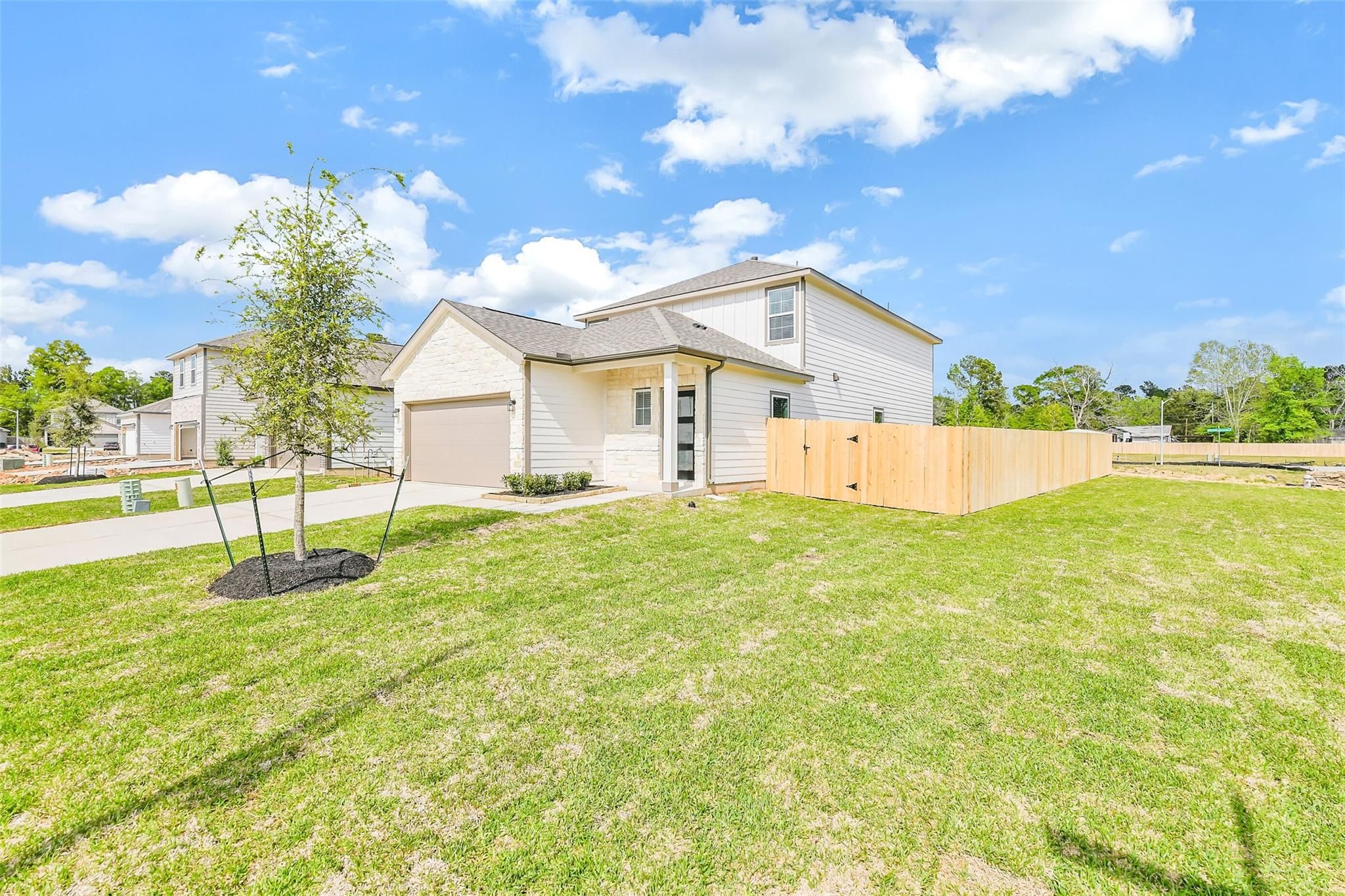 Two-story beige home with two-car garage, covered porch, and fenced yard in Caney Creek Place, Conroe, Texas