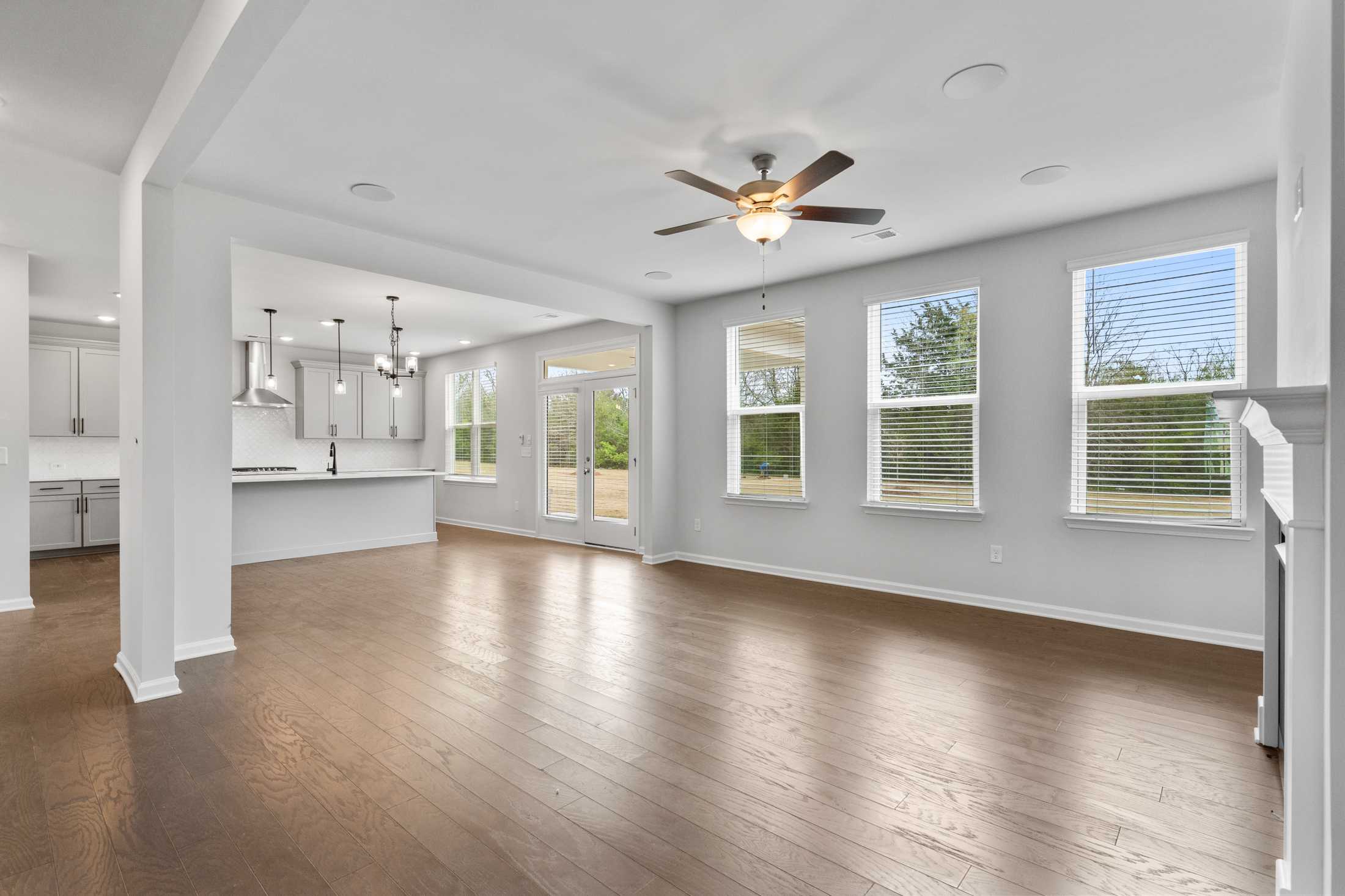 Spacious open-concept living and kitchen at Reverie at East Lake in McDonough GA with hardwood floors, ceiling fans, and large windows