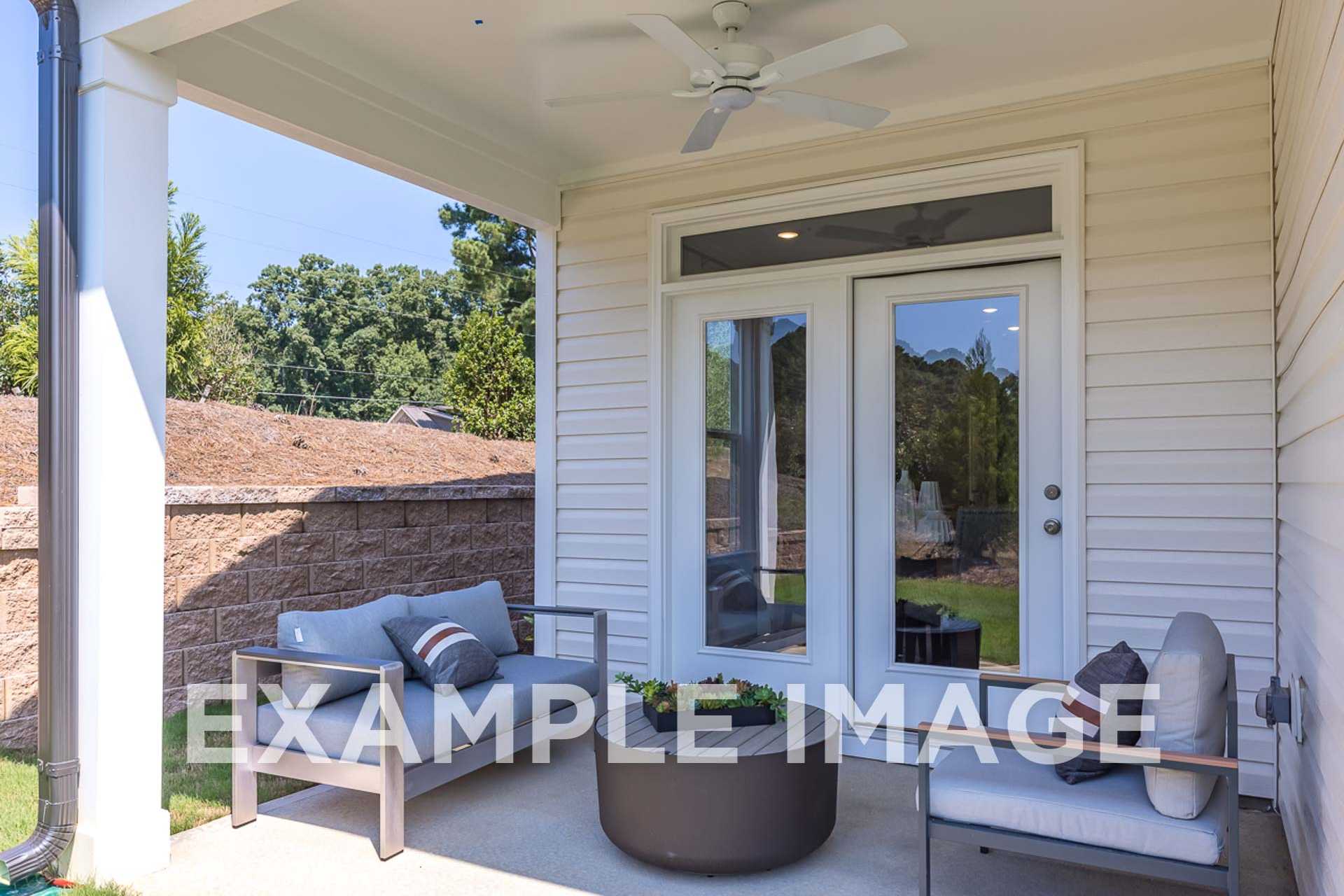 Spacious covered patio of The Ash E home with beige outdoor sofa, plants, French doors, and white siding exterior