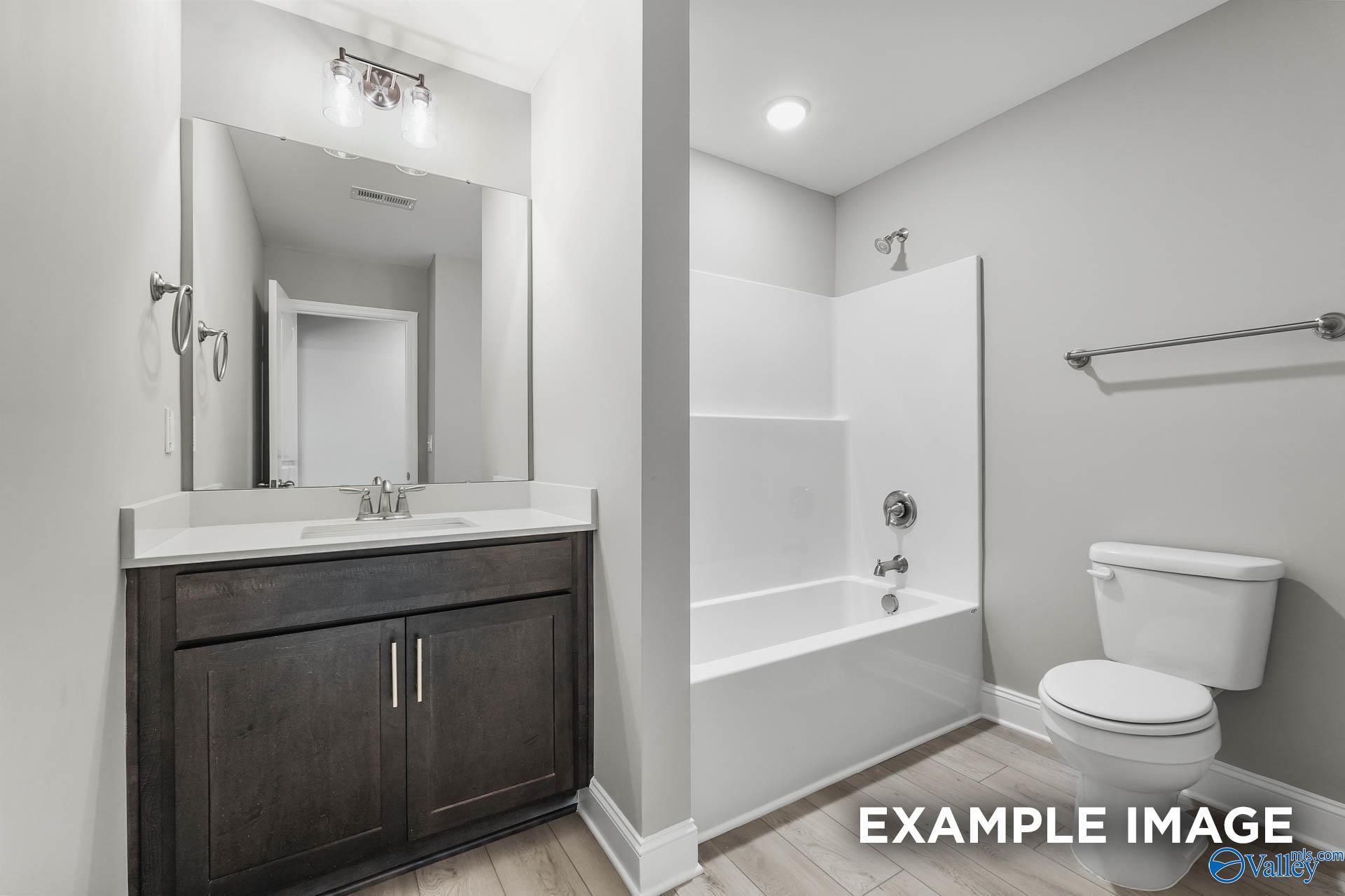 Modern bathroom with dark wood vanity, white tub-shower combo, and toilet in Davidson Homes The Everett B, Toney, Alabama