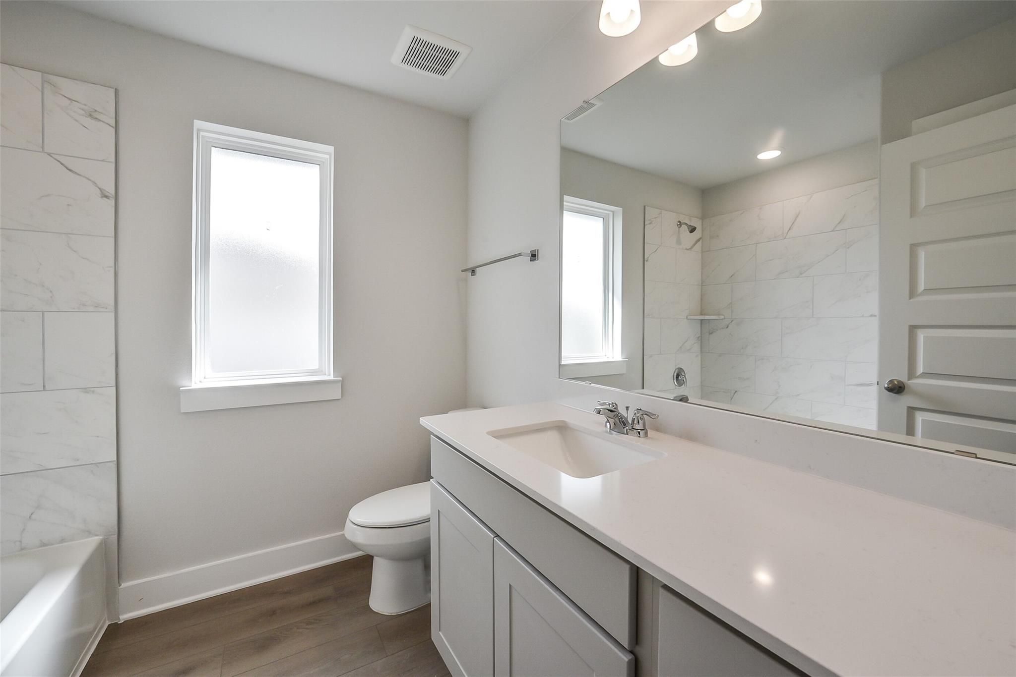 Modern bathroom with subway tile shower, white quartz vanity, large mirror, and frosted window in Davidson Homes The Philip B, Rosharon, Texas