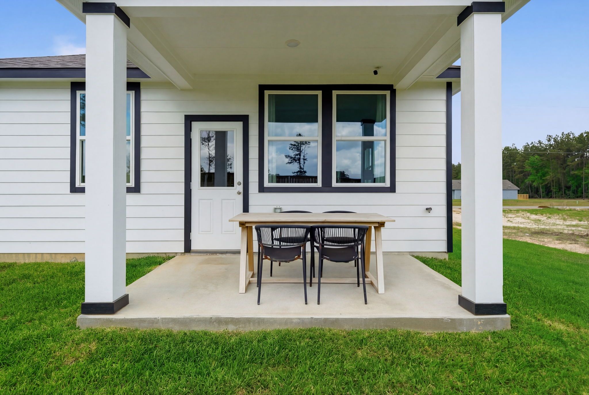 Covered porch at Spring Branch Crossing in Conroe Texas with wooden dining table chairs on concrete patio and green lawn