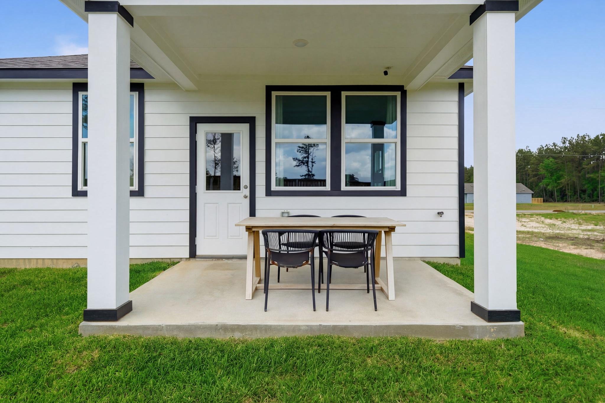Covered porch at Spring Branch Crossing in Conroe Texas with wooden dining table chairs on concrete patio and green lawn