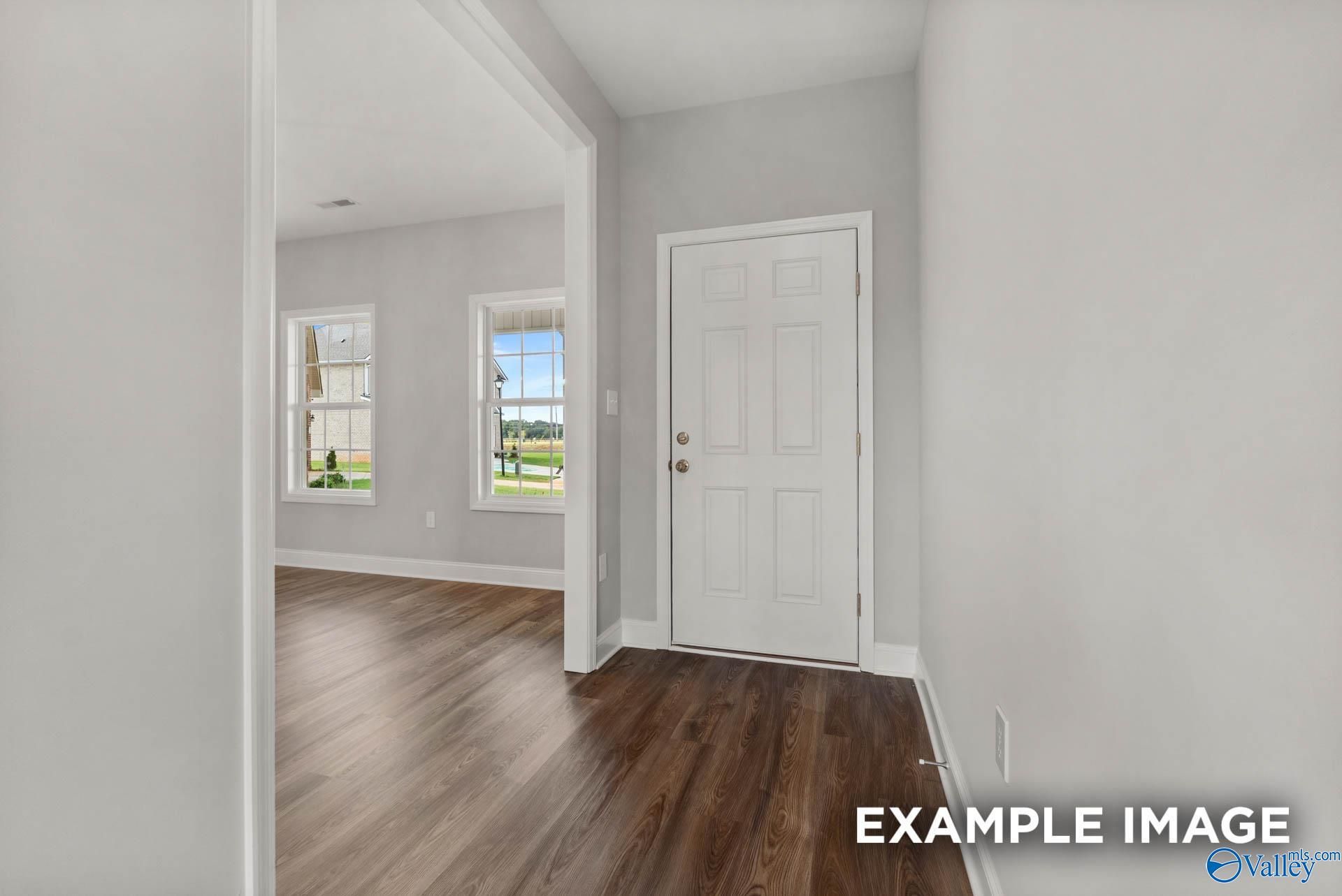 Bright hallway with hardwood floors, white paneled door, and windows overlooking green yard in Davidson Homes Shelby B, Athens AL