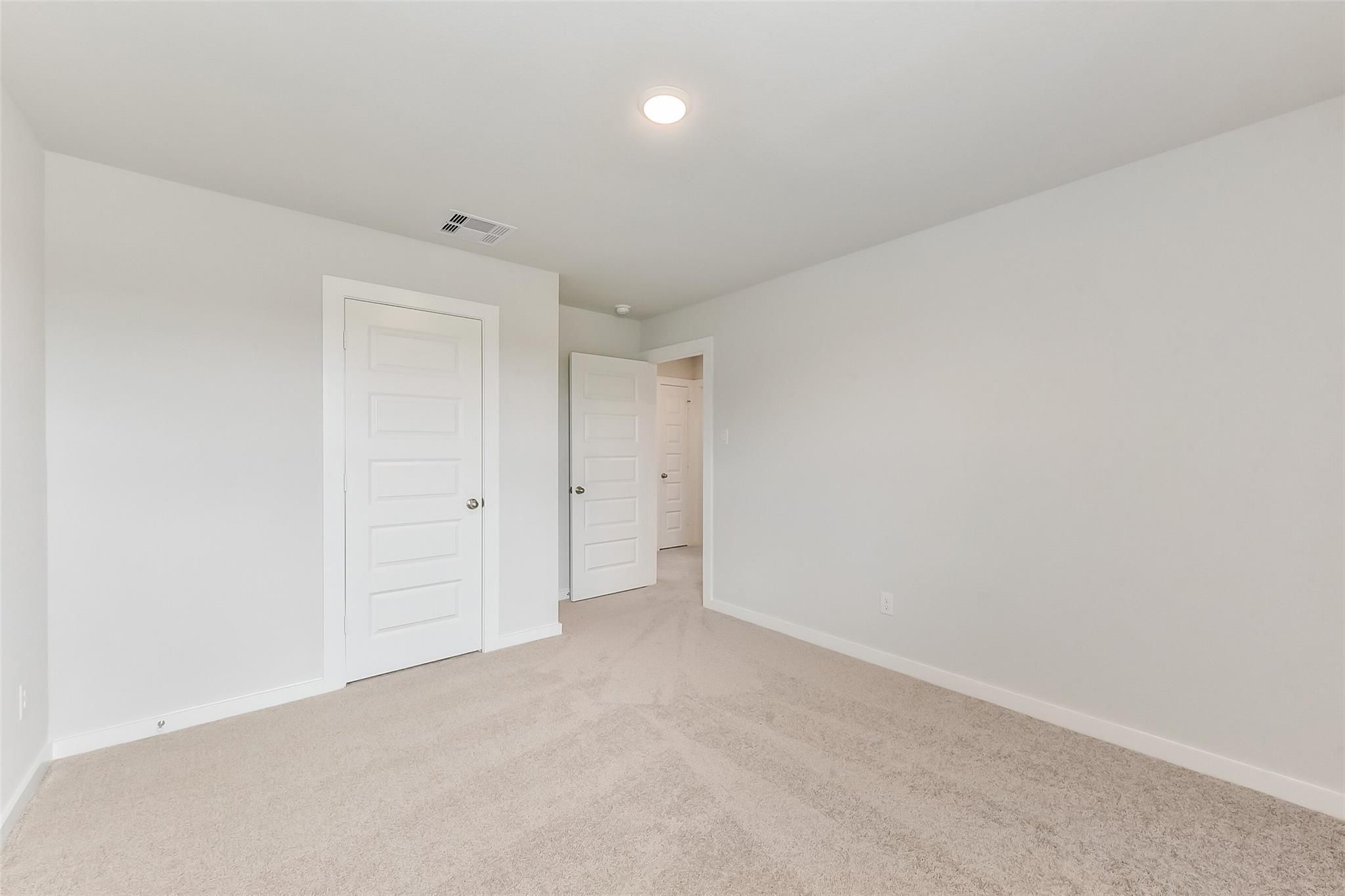 Empty bedroom with beige carpet, light gray walls, white doors to closet and bathroom in Davidson Homes Sabine F, Dayton Texas