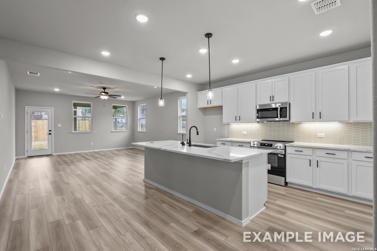 Open-concept kitchen with white cabinets and island in The Glenwood E floor plan at Royal Crest, San Antonio, Texas.