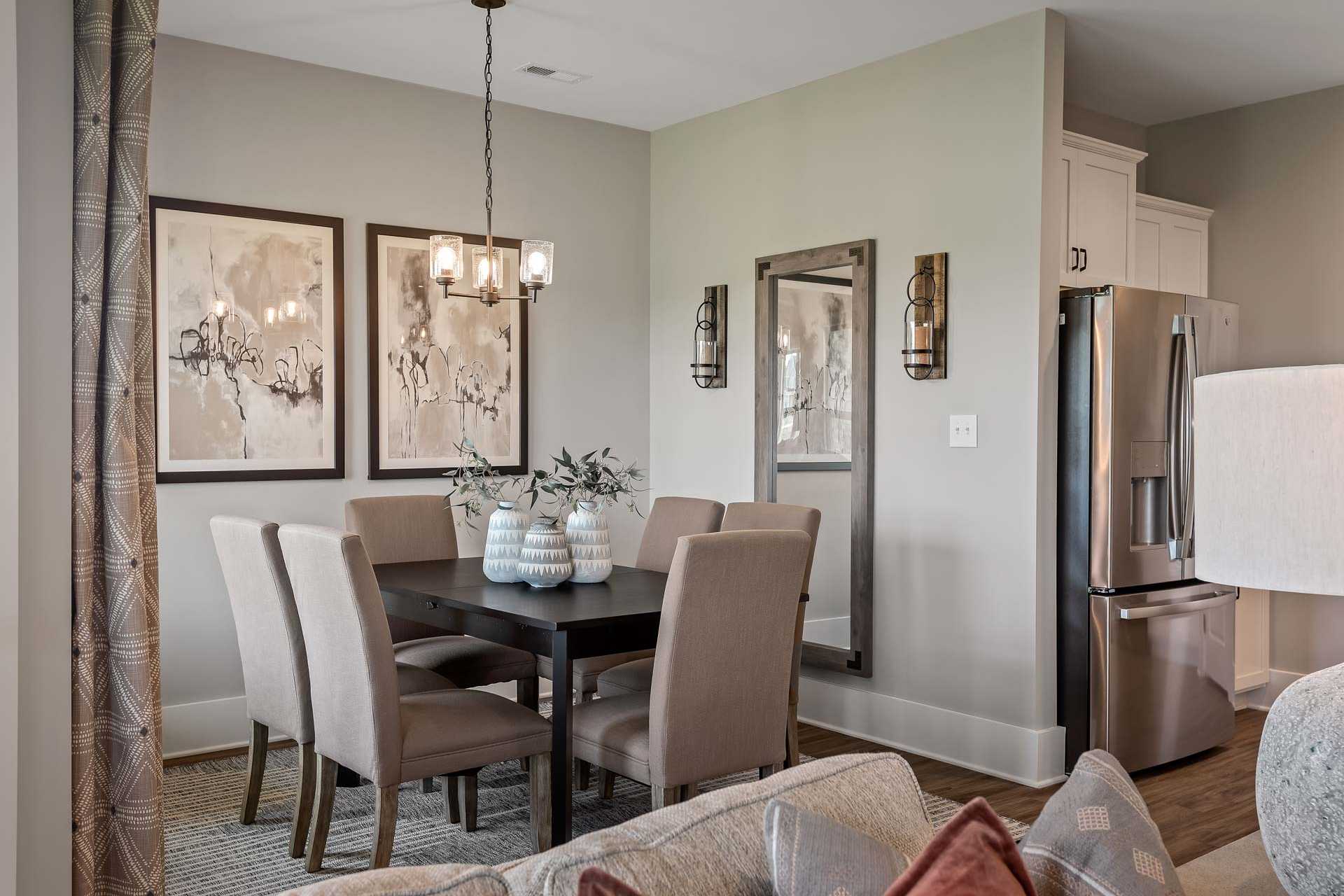 Spacious dining room at Heritage Lakes in New Market AL with wooden table, beige chairs, abstract art, pendant light, and open kitchen