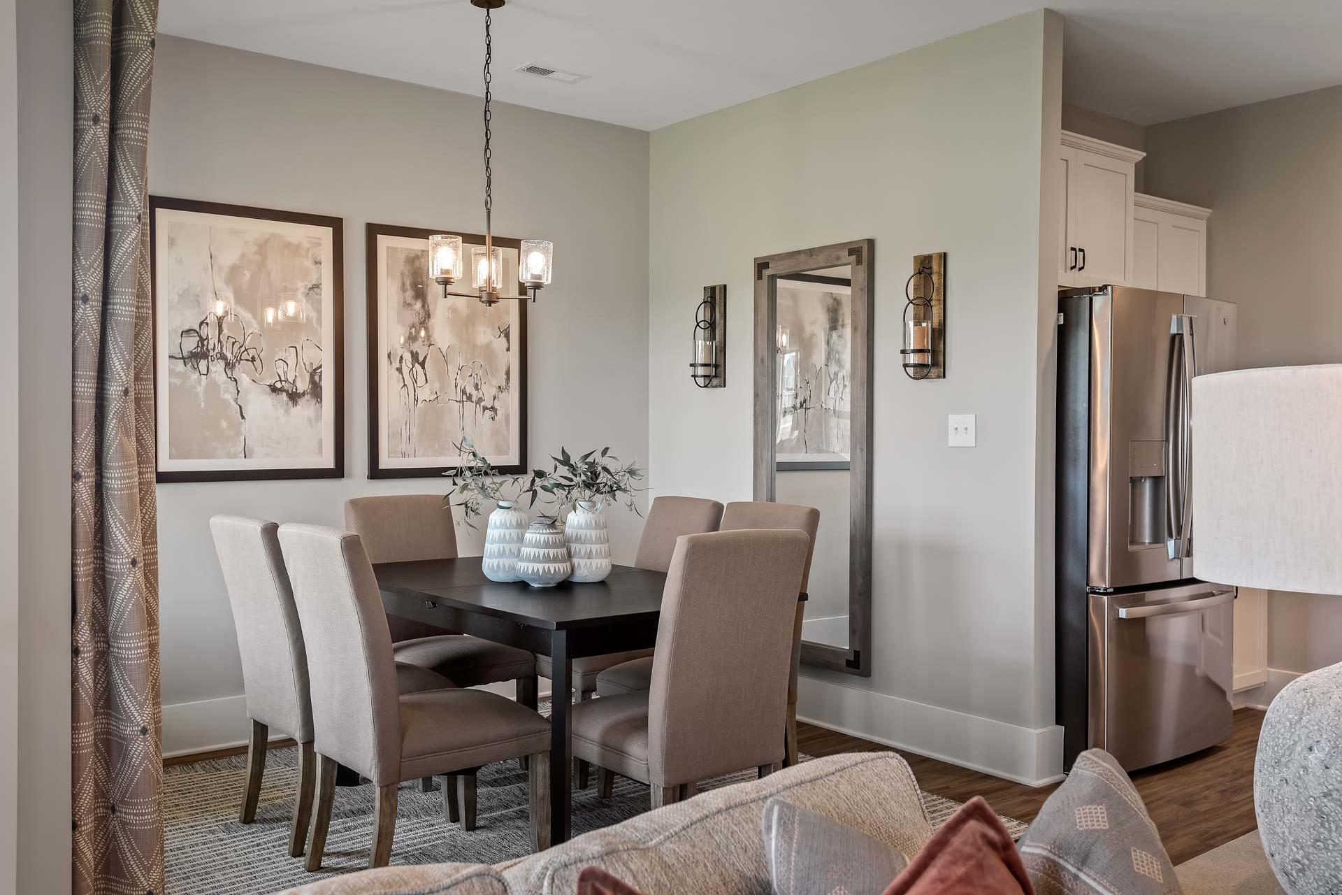Spacious dining room at Heritage Lakes in New Market AL with wooden table, beige chairs, abstract art, pendant light, and open kitchen