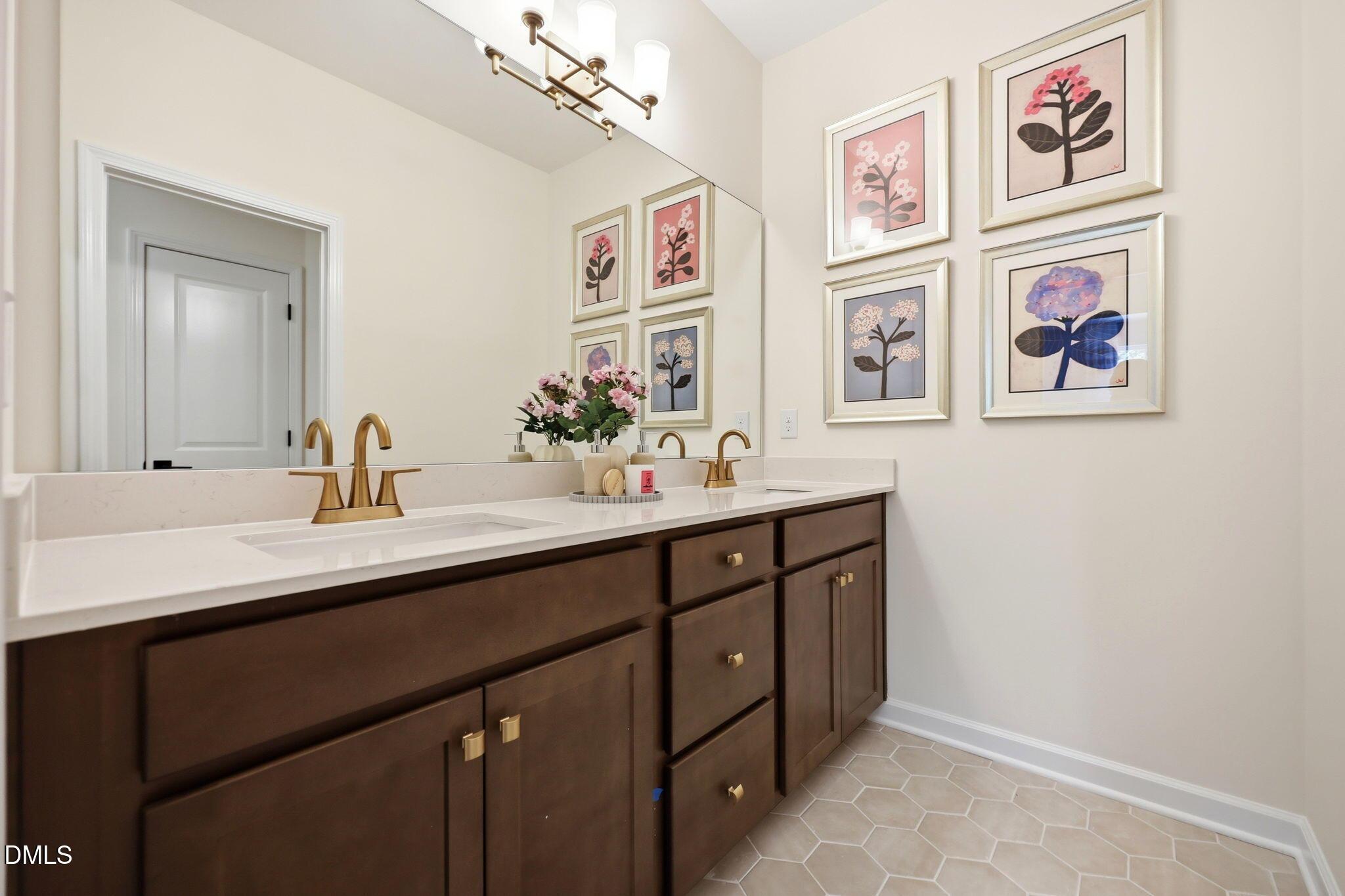 Double vanity bathroom with dark cabinets, gold hardware, and floral wall art in The Aspen B at Wendell Ridge, NC.