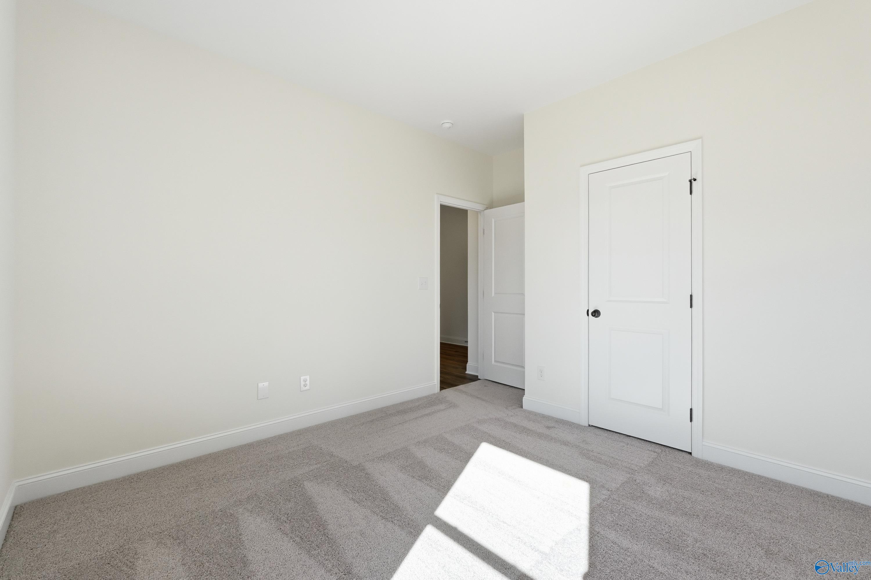 Bright empty secondary bedroom with beige walls, gray carpet, and adjacent closet in Davidson Homes The Franklin C, New Market, Alabama