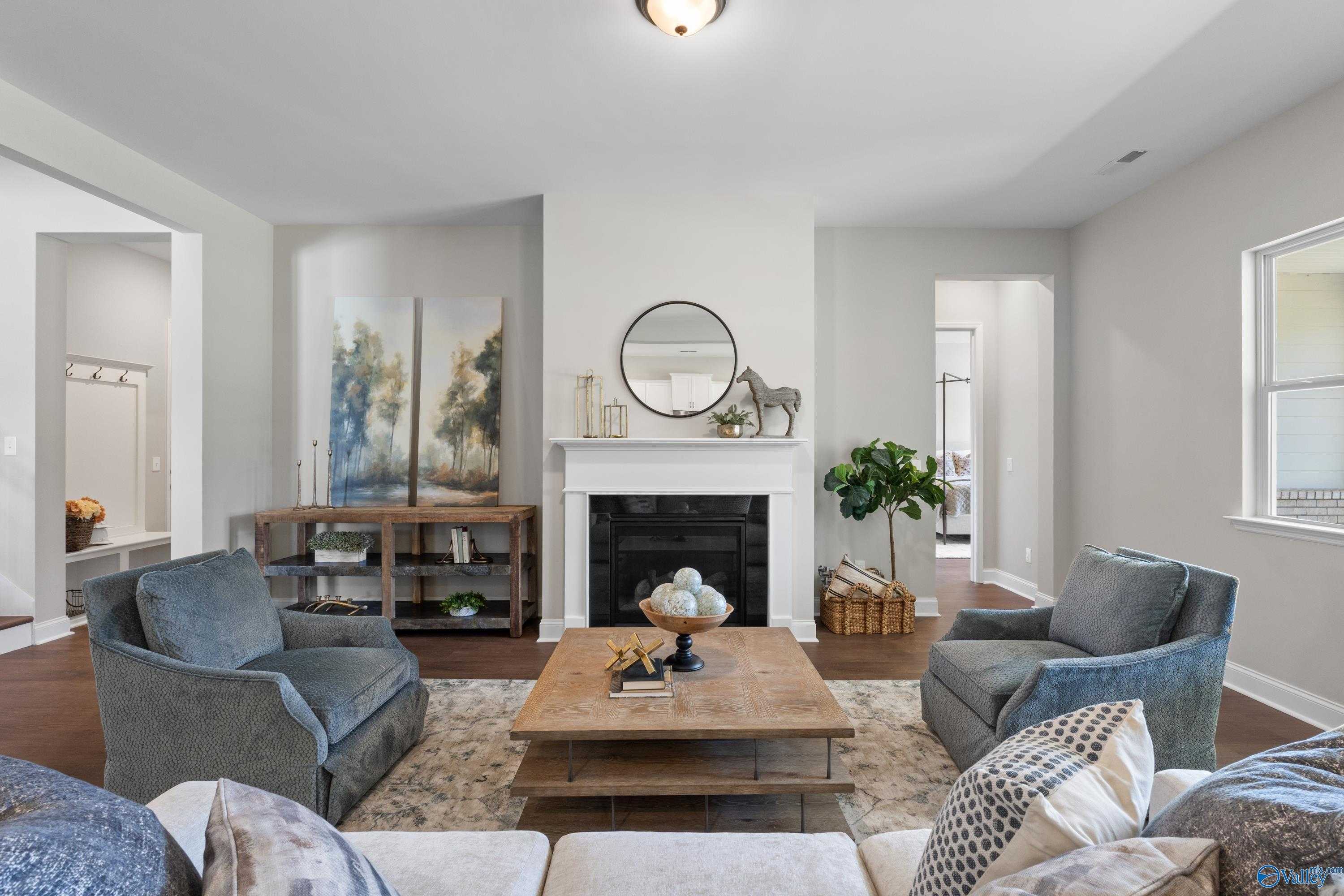 Cozy living room with white brick fireplace, blue velvet armchairs, and wooden coffee table in Evermore Homes The Haven, Owens Cross Roads, Alabama