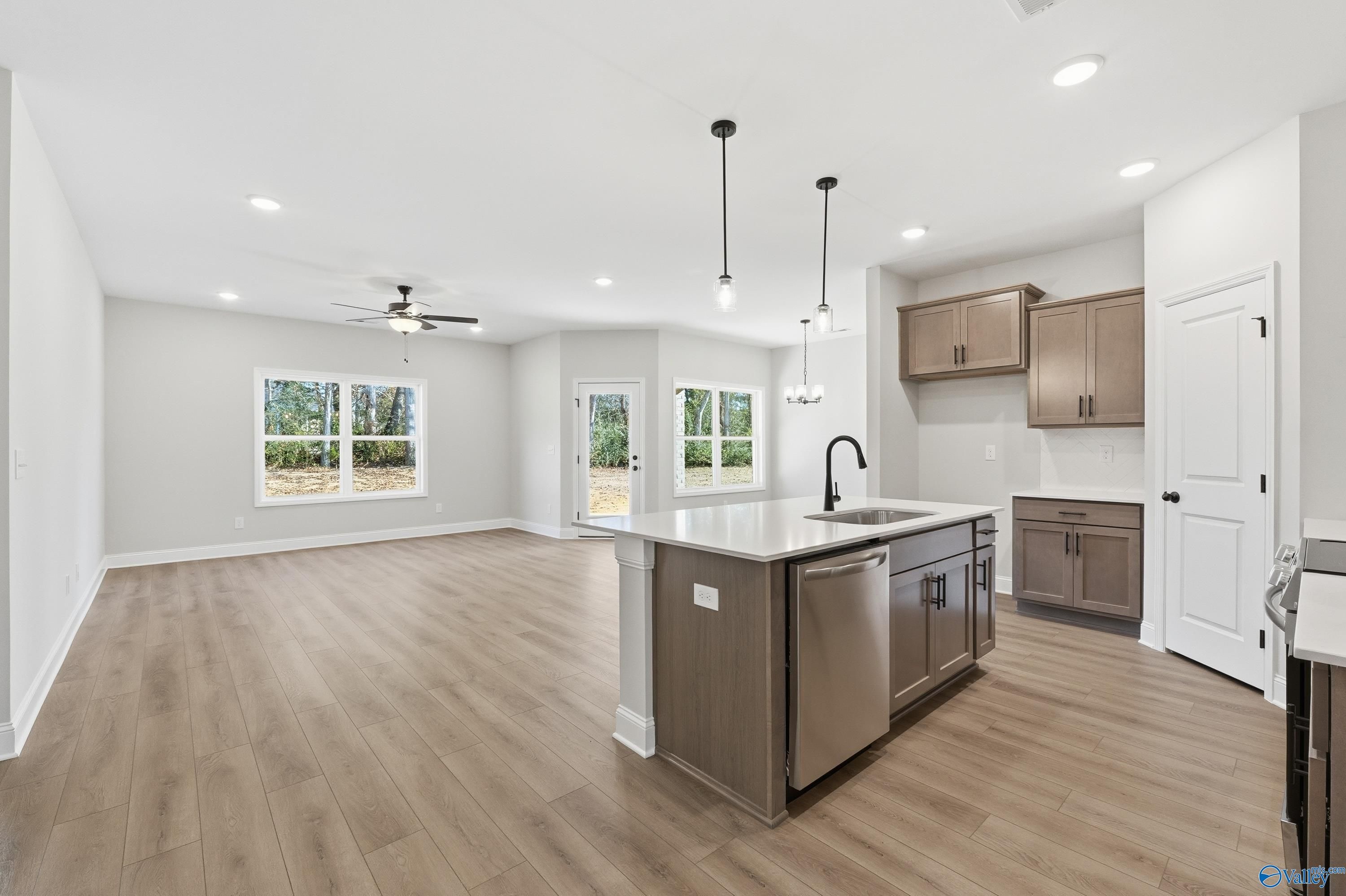 Modern open-concept kitchen with large island, stainless steel sink, wood cabinets, and backyard view in Davidson Homes The Daphne C, New Market, AL