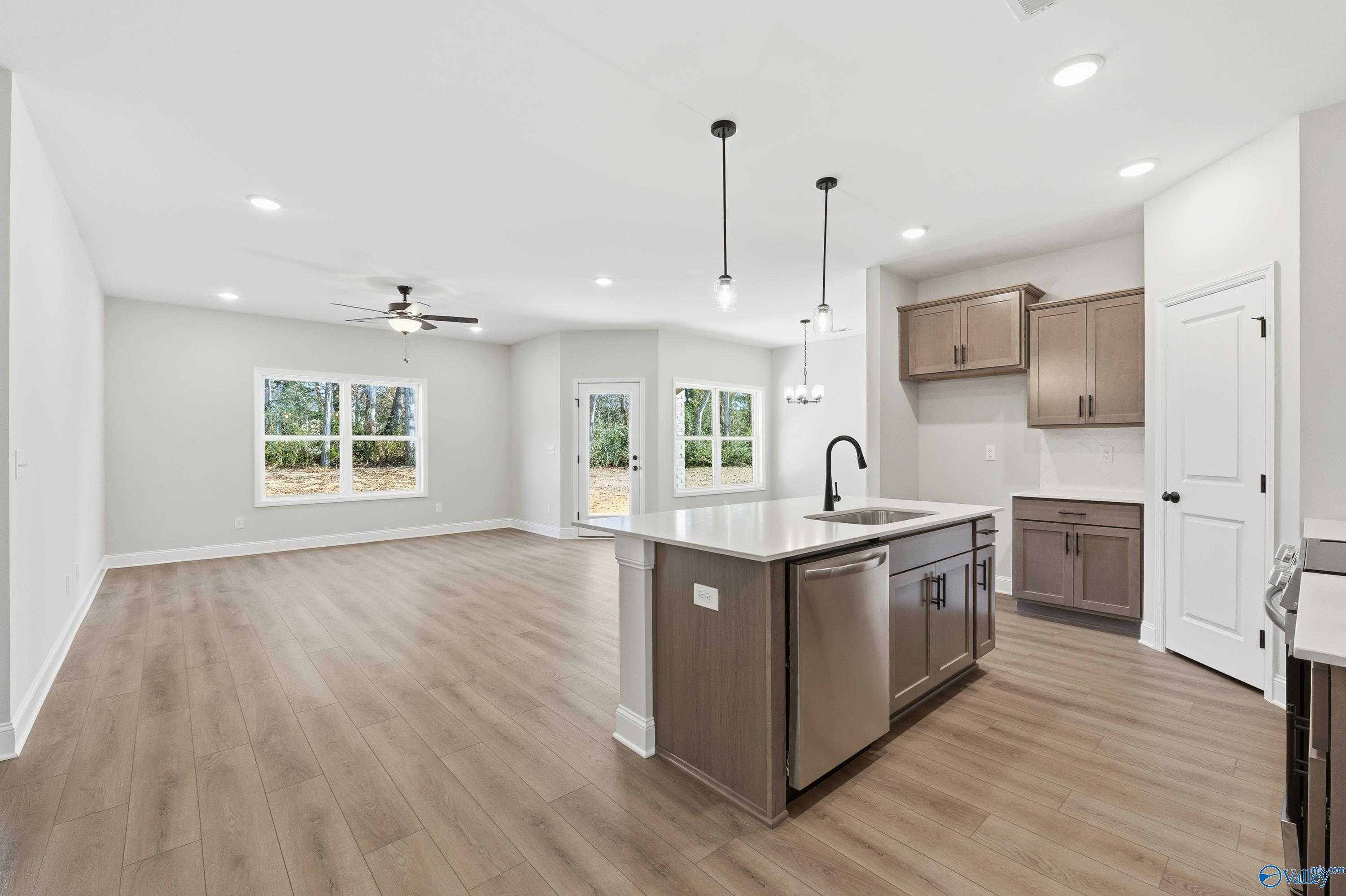 Modern open-concept kitchen with large island, stainless steel sink, wood cabinets, and backyard view in Davidson Homes The Daphne C, New Market, AL